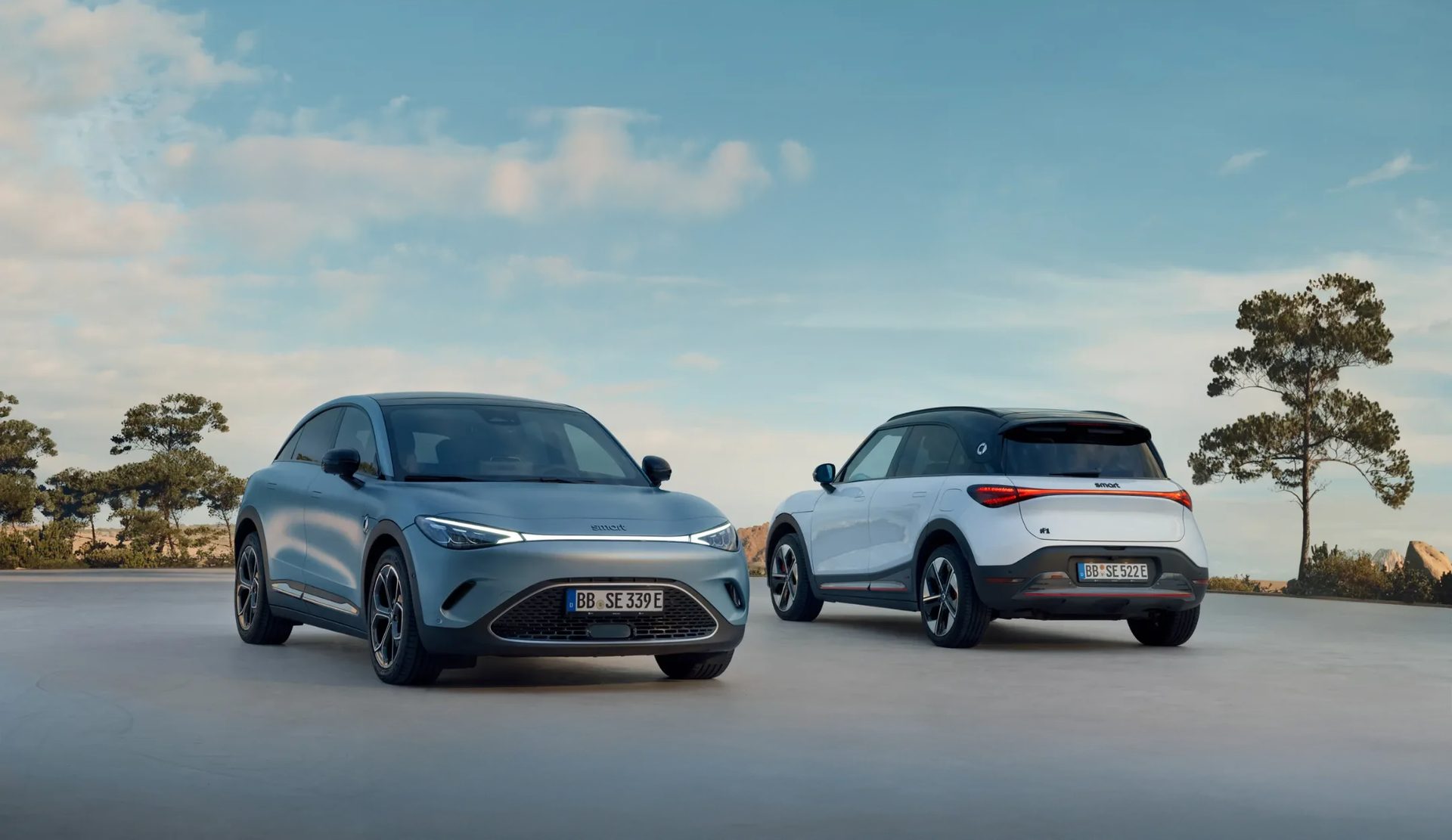 Two Smart SUVs: gray facing front, white facing rear, parked outdoors.