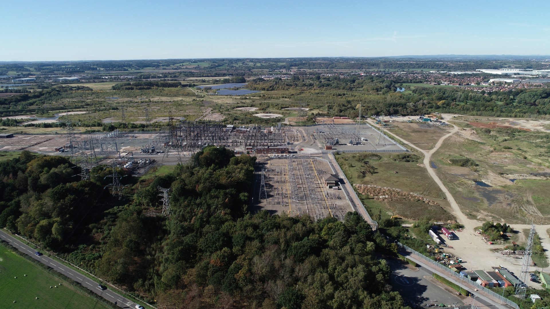 Aerial view of a large electrical substation complex with numerous power lines and pylons in a rural landscape.