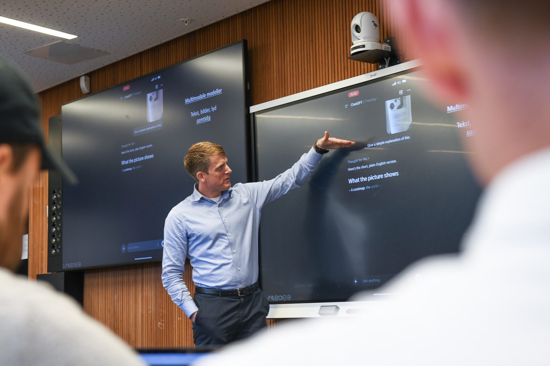 Man in blue shirt presenting AI content on large screens, explaining 'Multimodal models'.