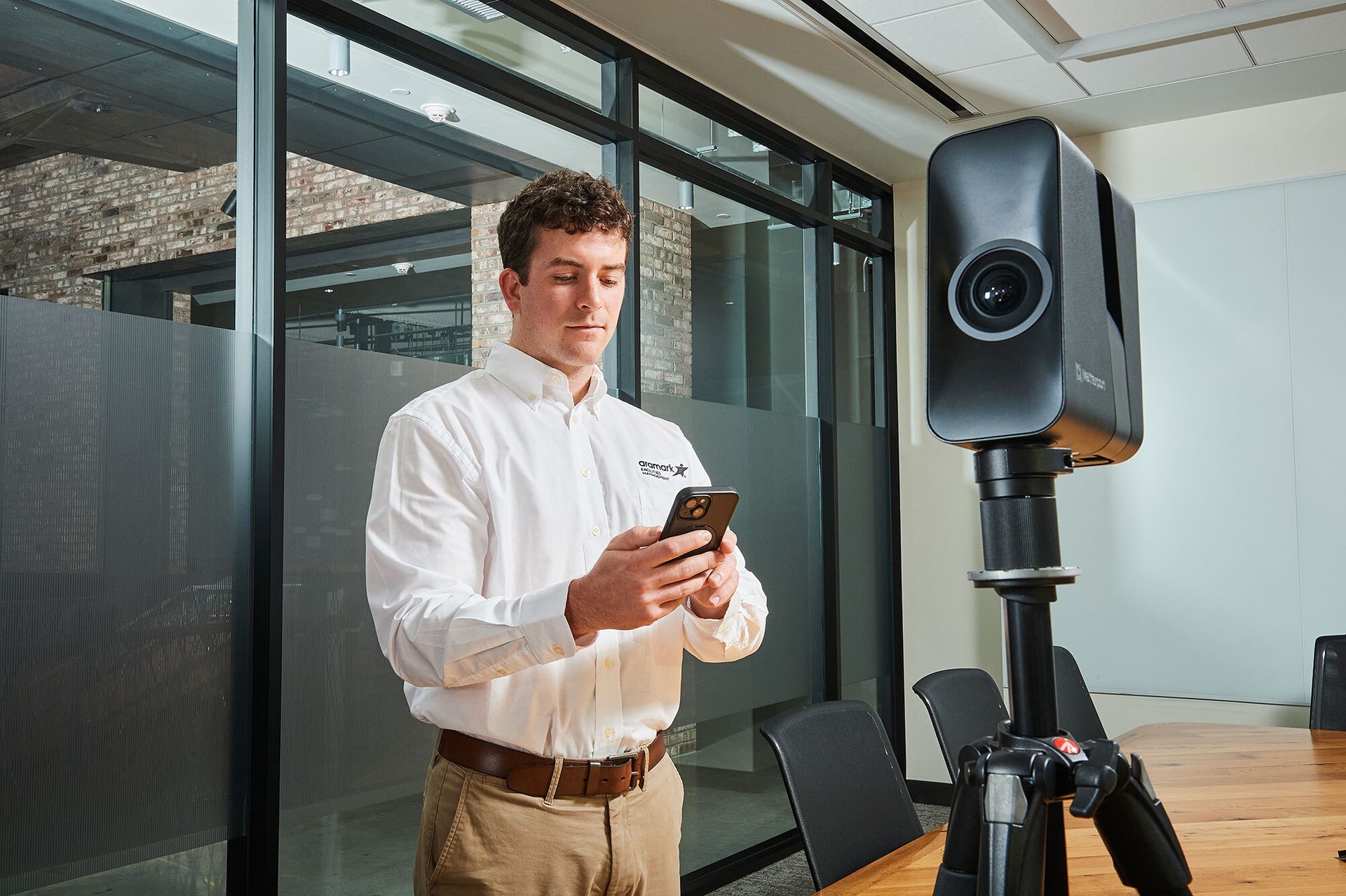 Man on phone next to tripod-mounted camera in an office.
