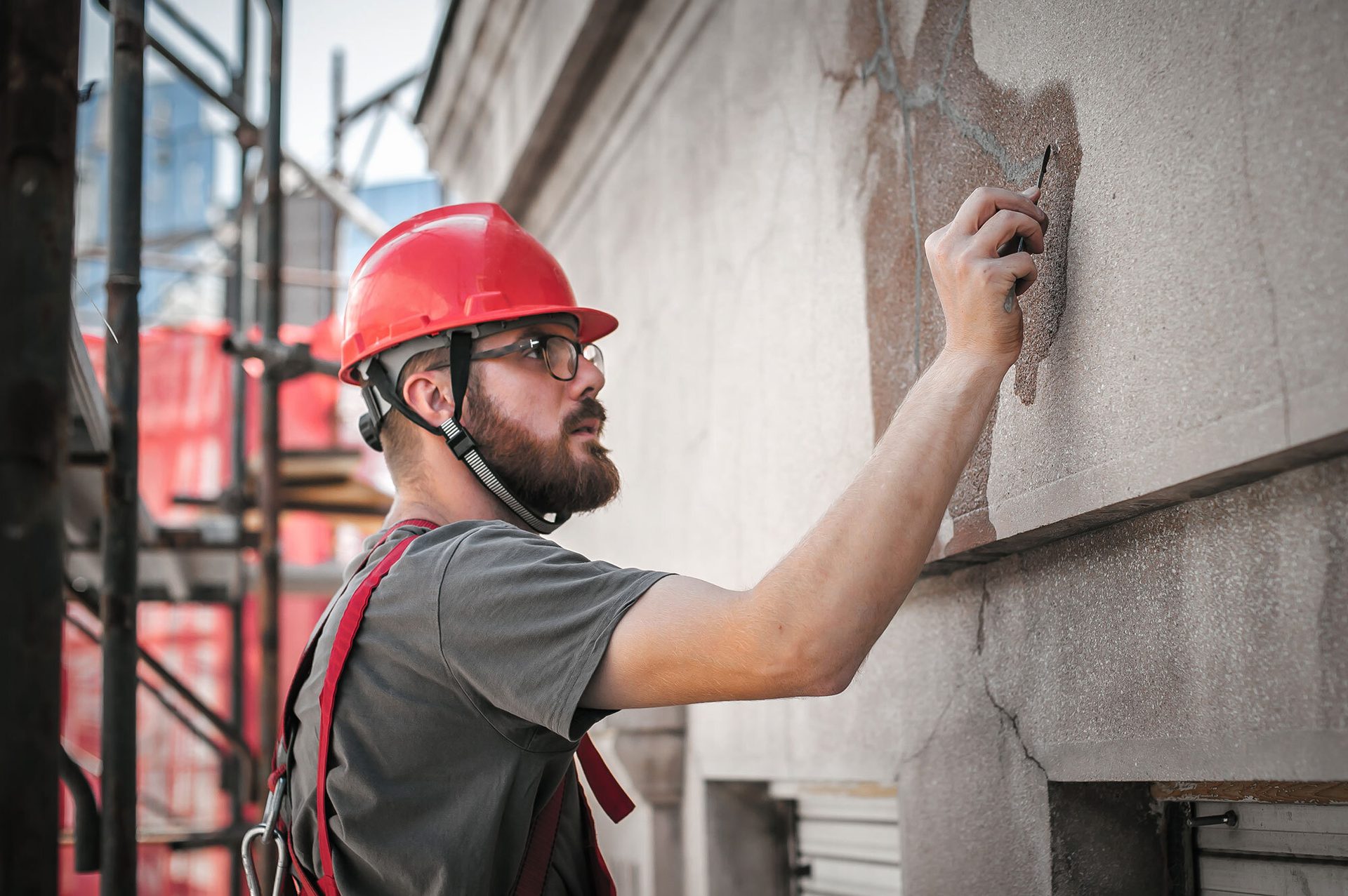 Worker in red hard hat and harness details building wall.