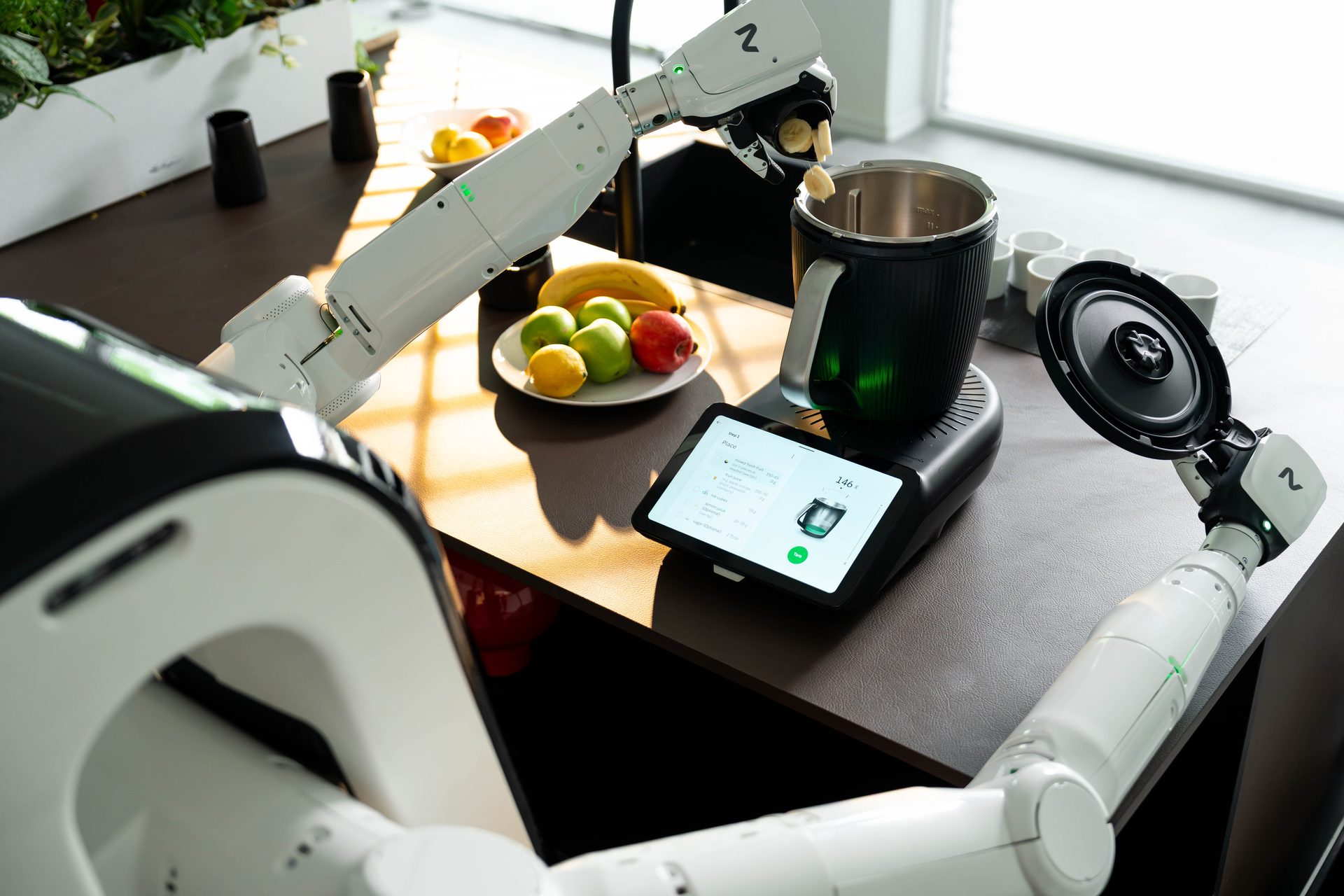 Robot arm places fruit in blender next to fruit plate and tablet.