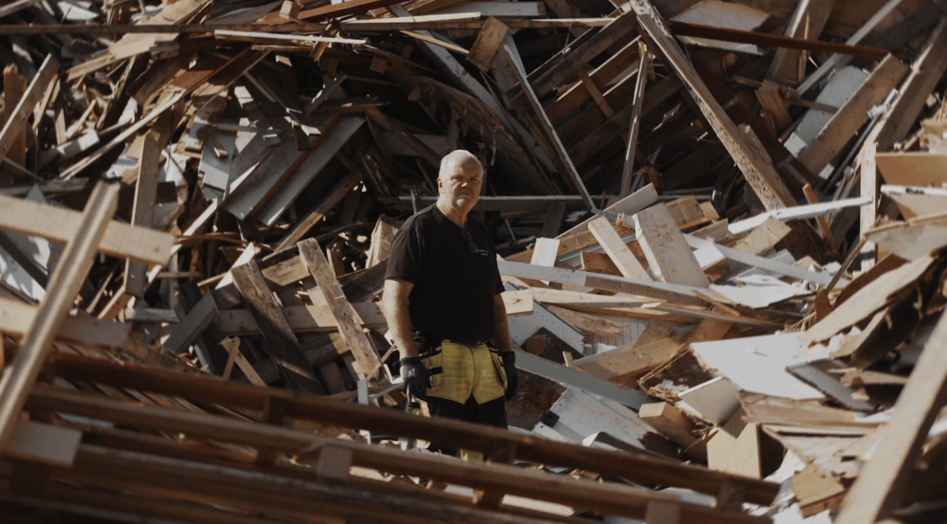 Man standing in a huge pile of wooden debris.