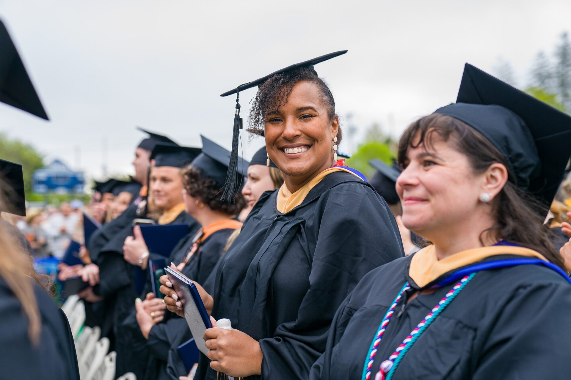 Facial expression, Academic dress, Social group, Clothing, Smile, Mortarboard, Scholar, Graduation, Gesture, Interaction