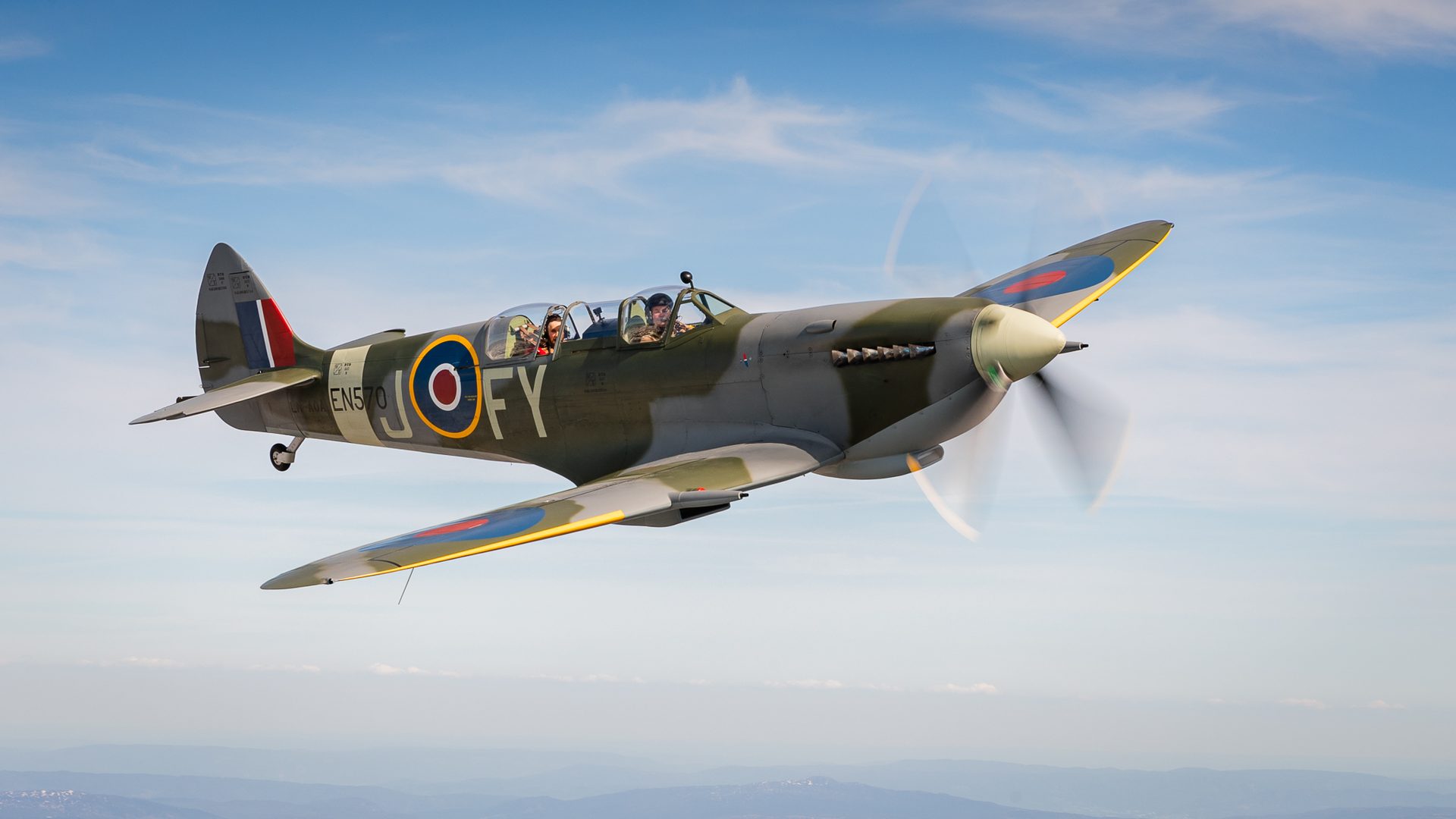 Spitfire airplane flying with two people aboard.