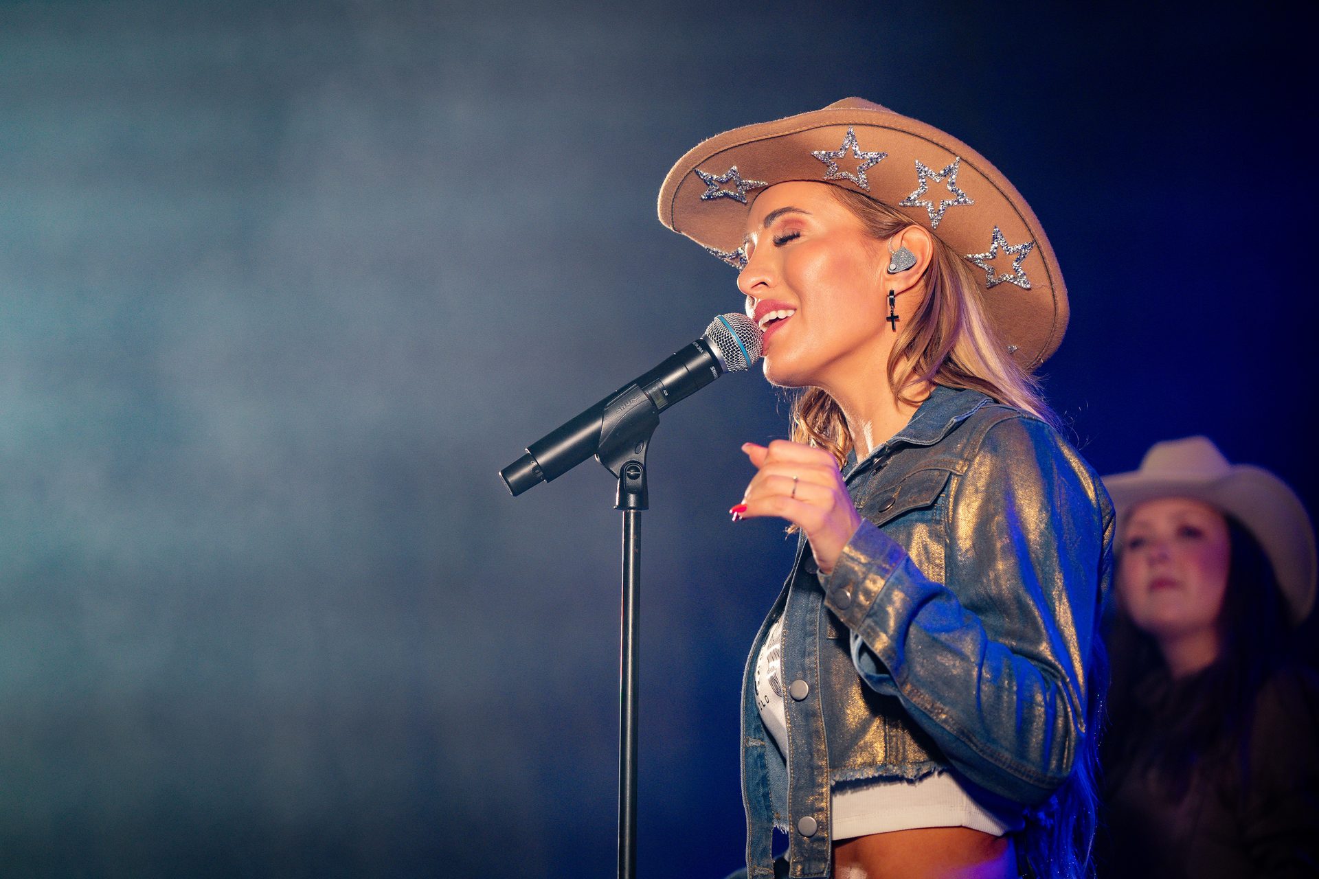 Singer in a cowboy hat singing into a microphone on stage.