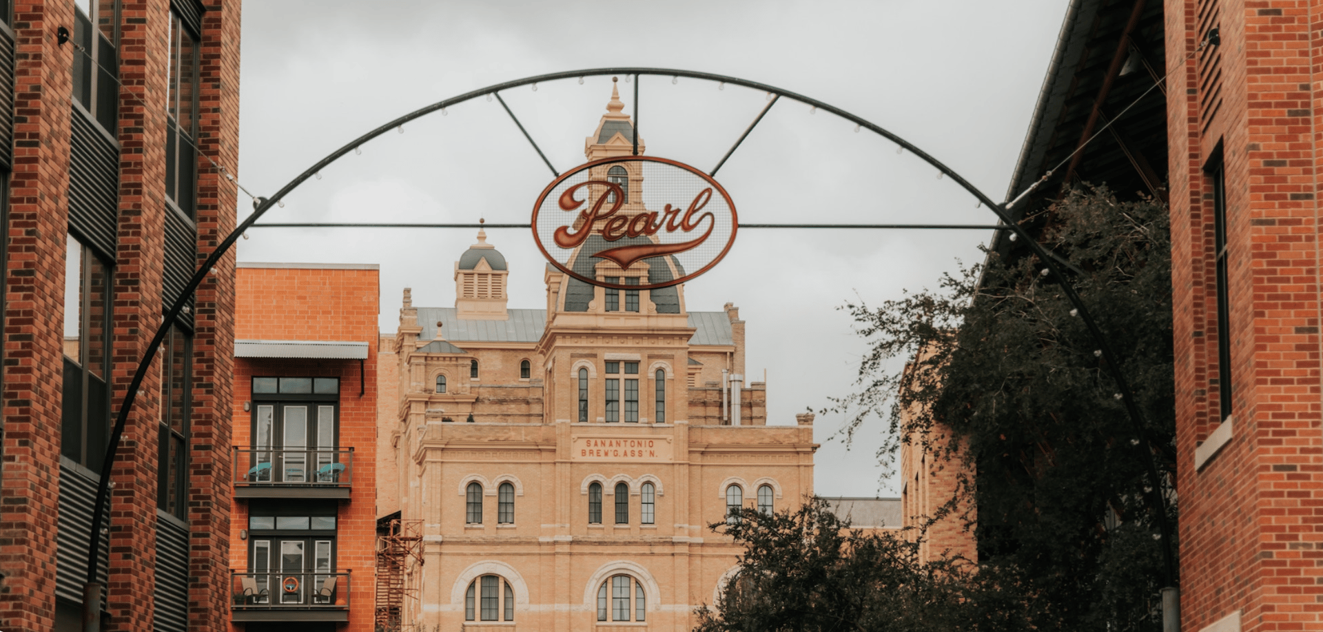 Pearl sign arching over a historic San Antonio brewery, flanked by modern brick buildings.