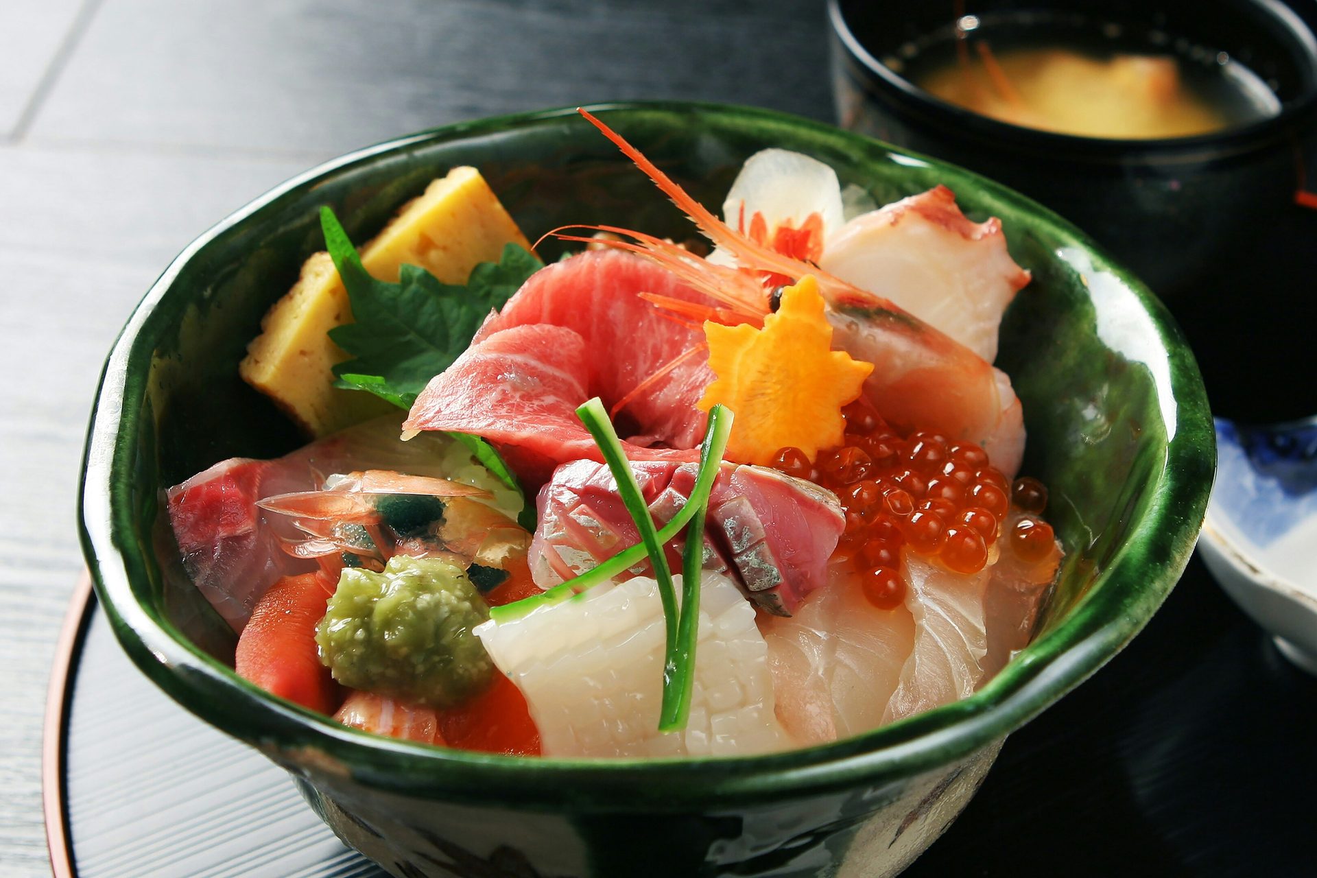 A colorful Japanese chirashi bowl with various fresh fish, shrimp, roe, and egg, served with miso soup.