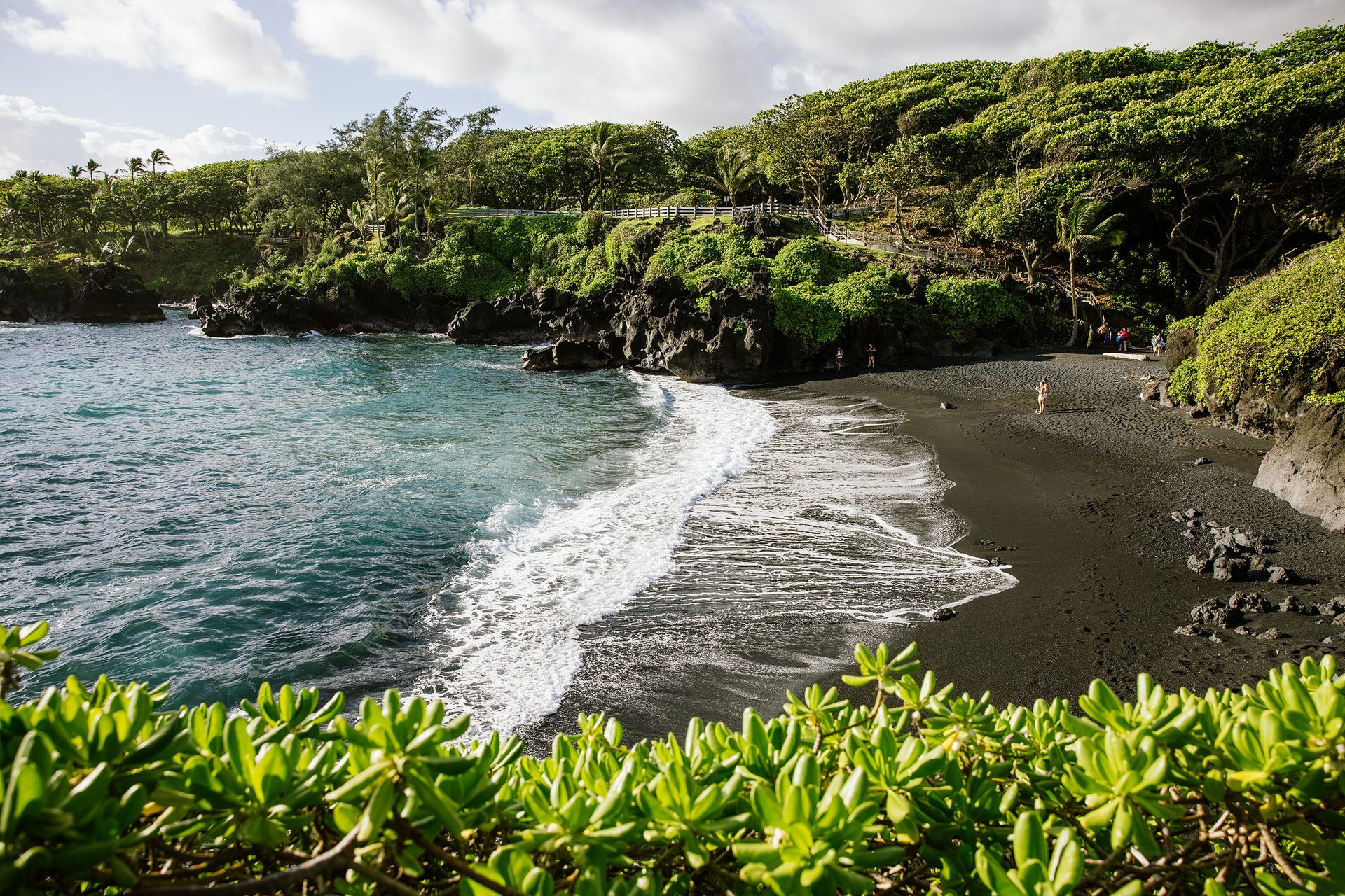 Black sand beach with waves, green hillside, and visitors.