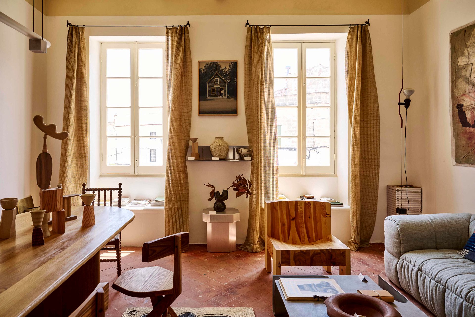 A warm room with terracotta floor, wooden furniture including a large table, and a light gray sofa.