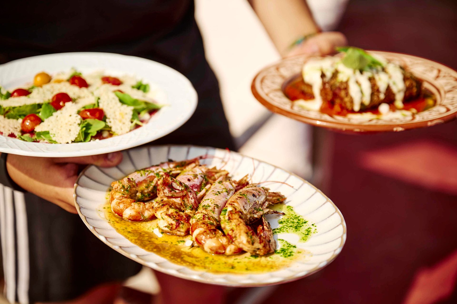 Three plates of food, including salad and grilled shrimp, held by people.
