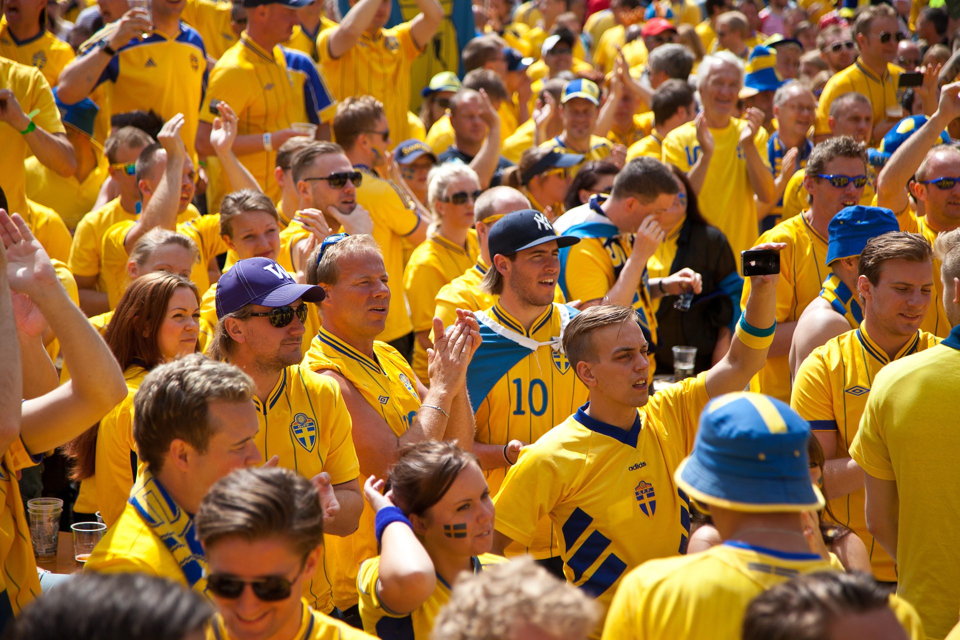 A large crowd of people wearing yellow and blue Swedish jerseys cheer at a sporting event.