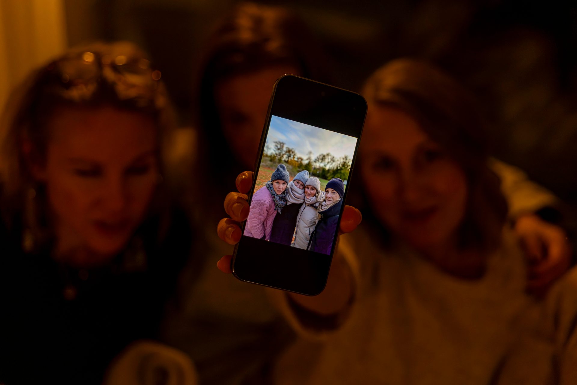Hand holding a smartphone displaying a photo of four women.