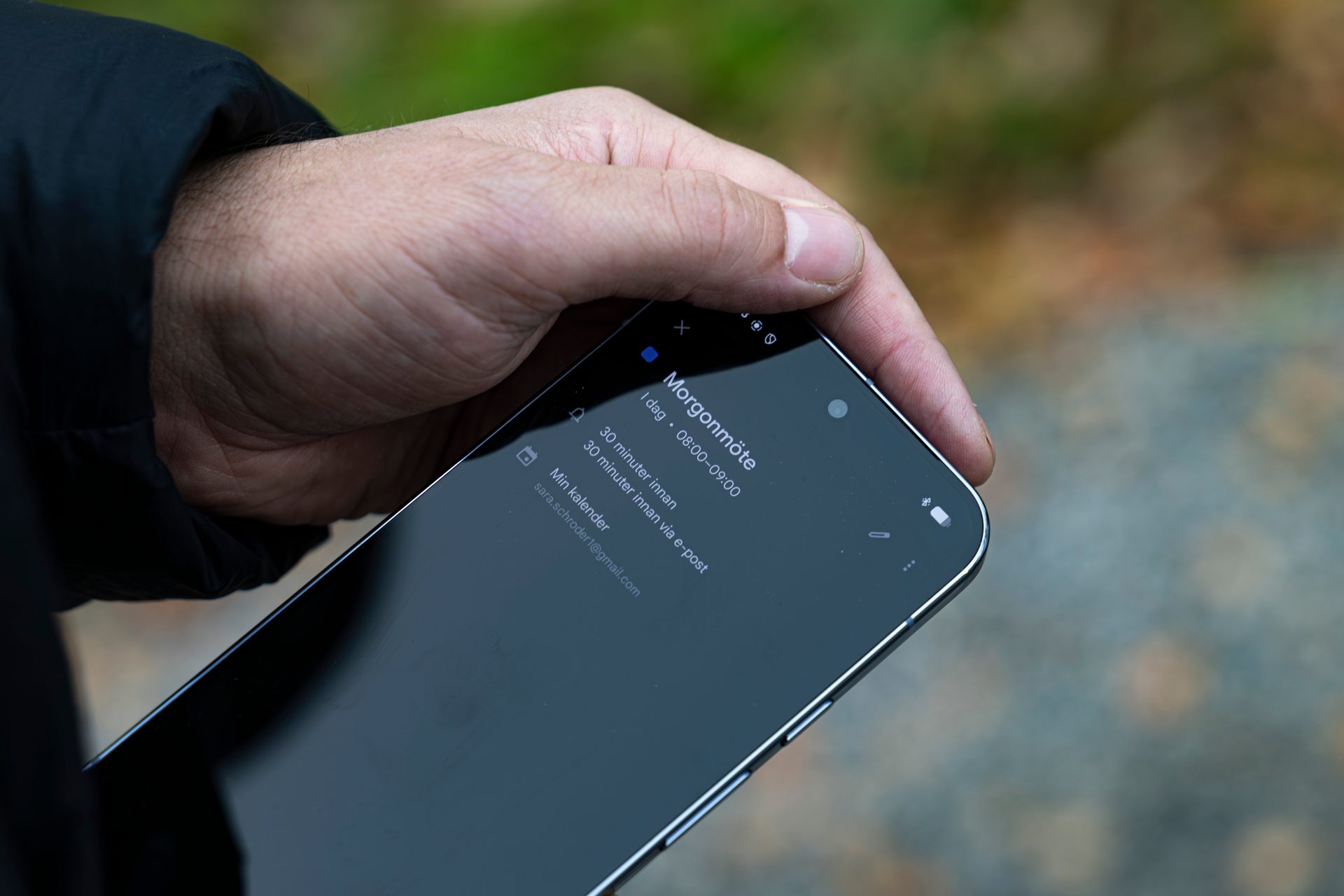 Hand holding a smartphone displaying a "Morgonmöte" (Morning meeting) calendar event.