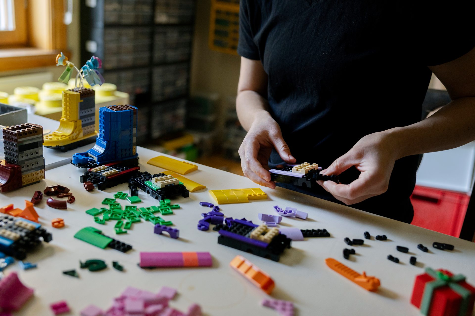Person building colorful LEGO creations on a white table, including flower-pot boots.