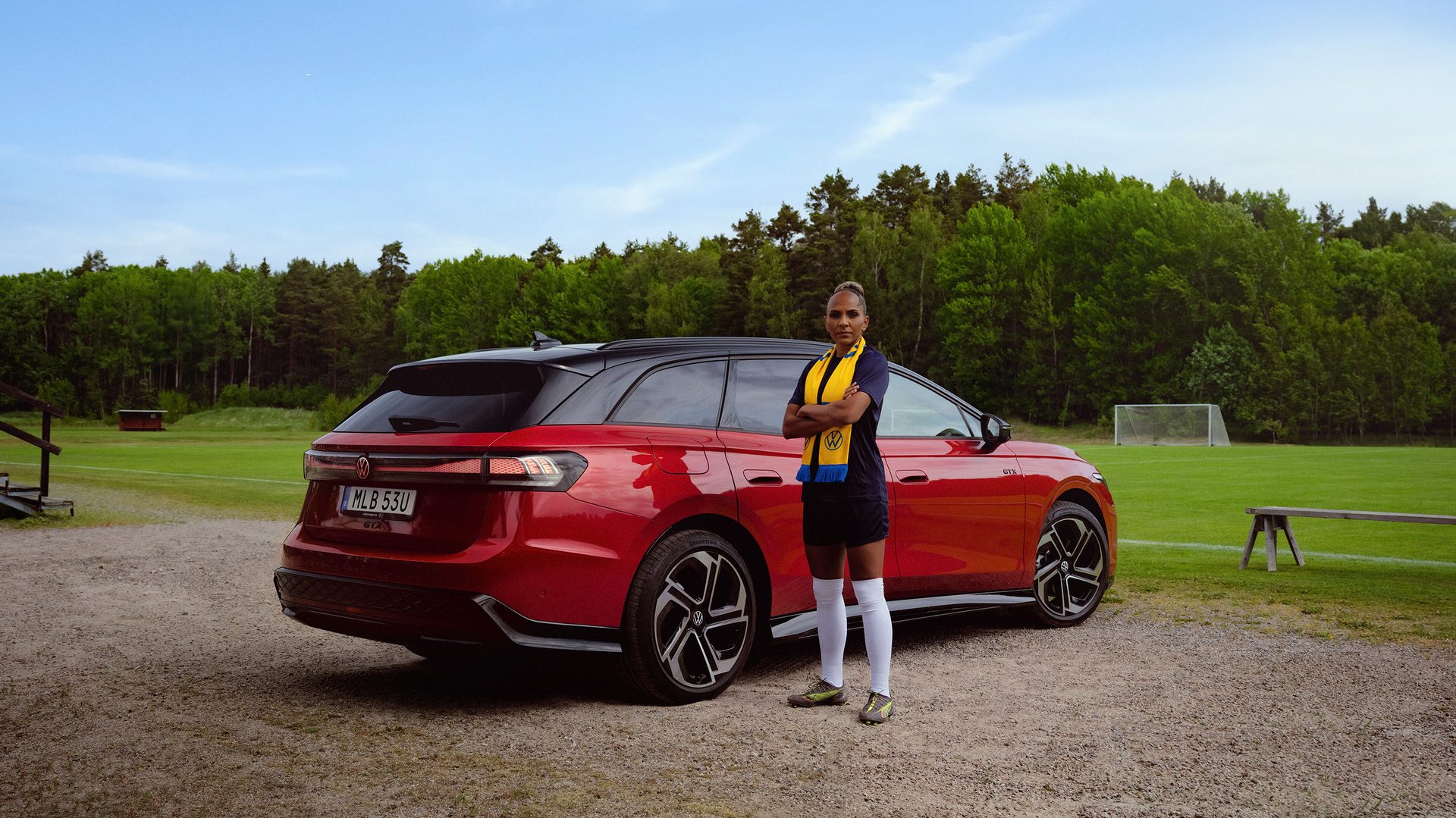 Soccer player with scarf next to red VW ID.7 GTX car on a soccer field.