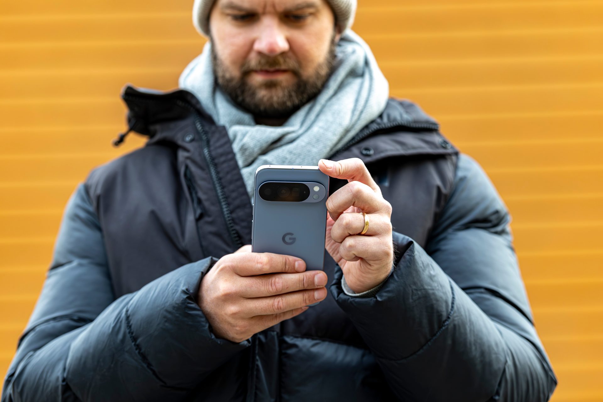 Man in winter clothes holding a Google Pixel phone against an orange background.