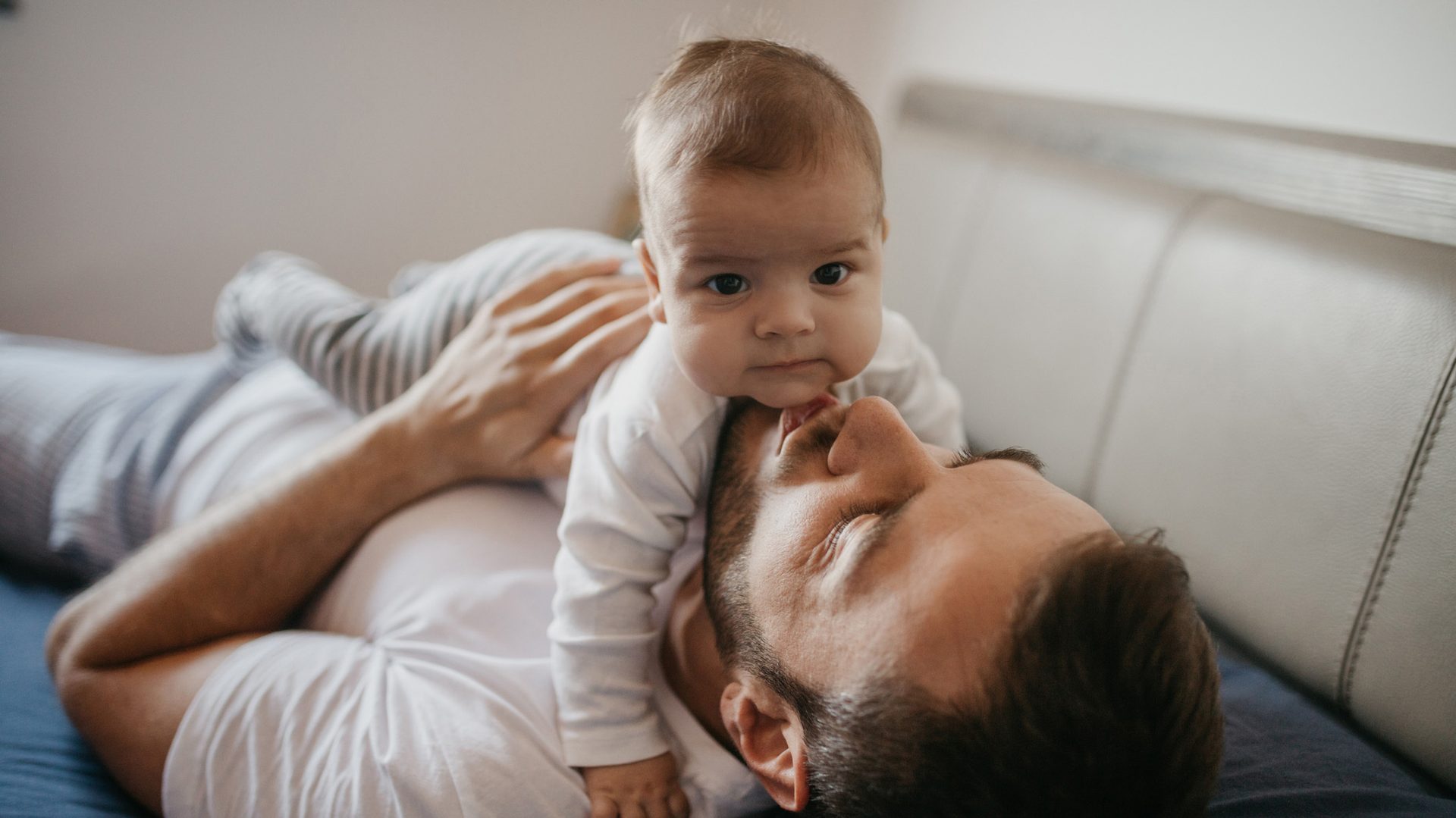 Baby lying on man's chest, chin touching his face, looking forward.