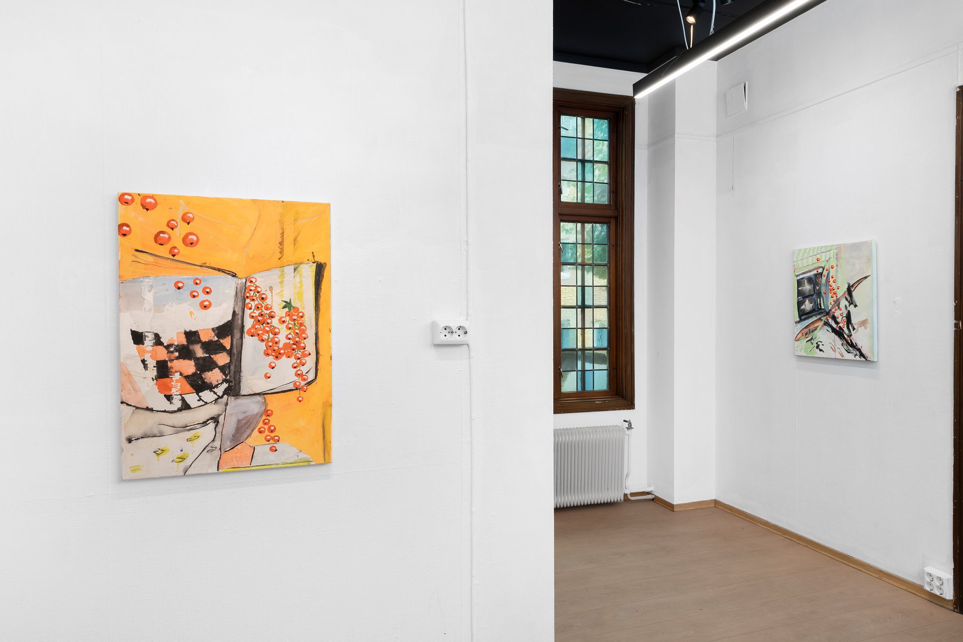 Art gallery interior with two paintings, a tall window, and a radiator on a white wall.