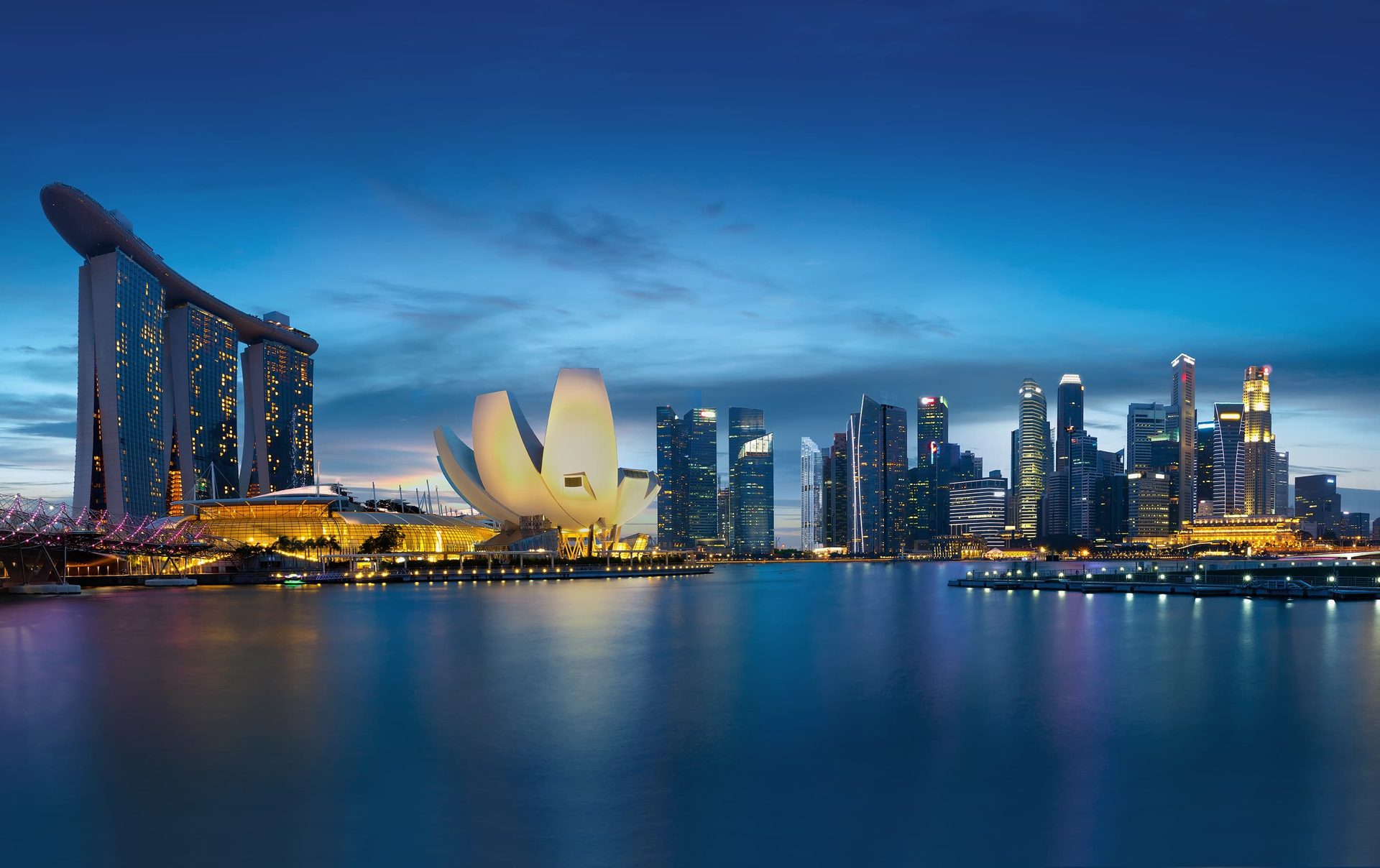 Singapore's Marina Bay at twilight with the illuminated skyline, Marina Bay Sands, and ArtScience Museum reflecting on the water.
