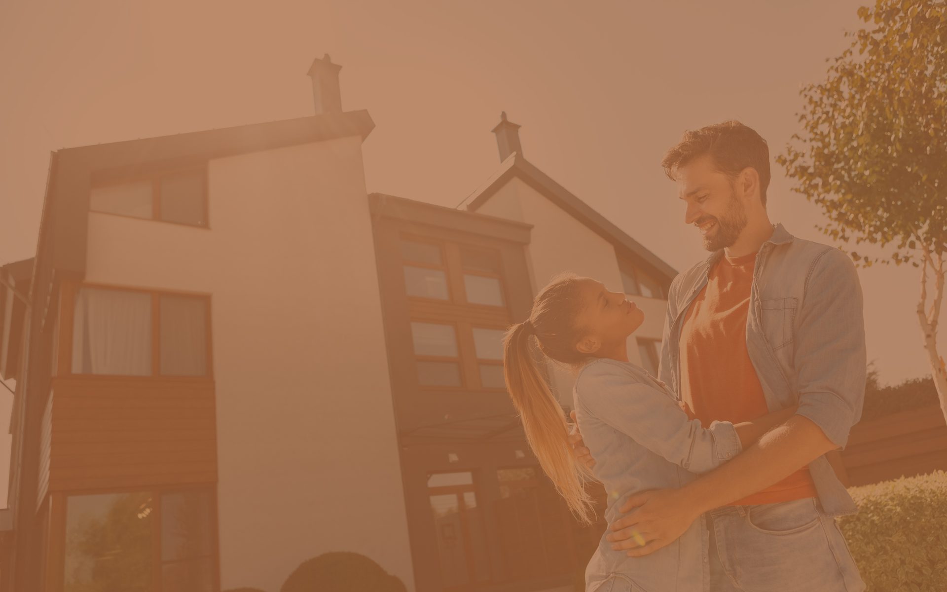 Tinted brown hues over the image of a young homeowner couple embracing and smiling in front of their home.