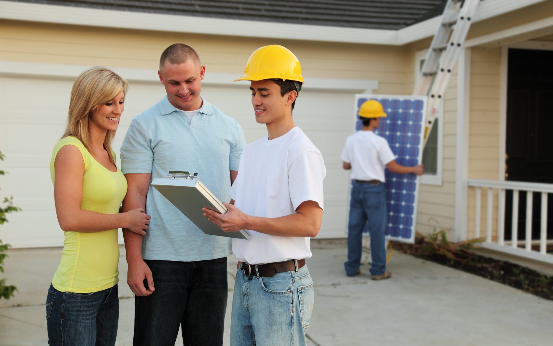 contractor wearing hardhat talking to homeowners while solar panels being installed in background