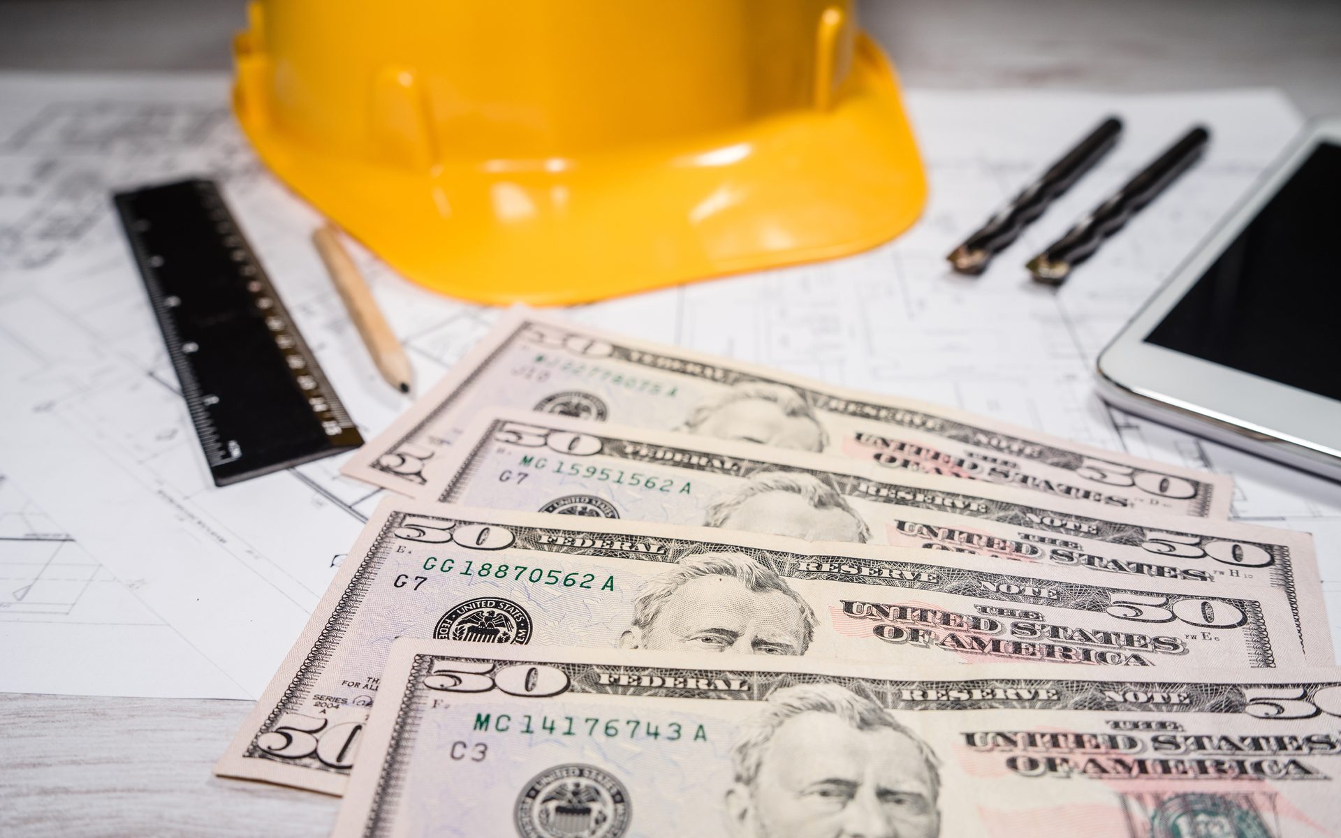 photo of a yellow hardhat on a table with contractor materials and cash bills