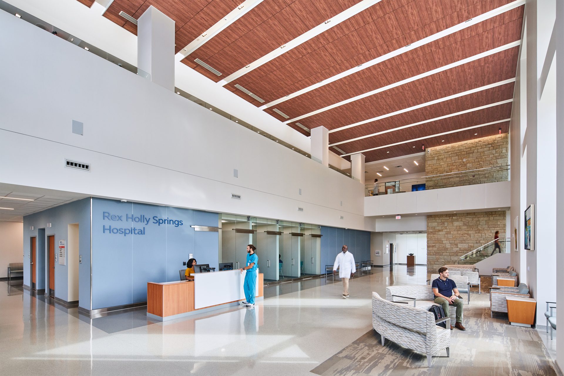 Hospital lobby interior with high wood finish ceiling system.