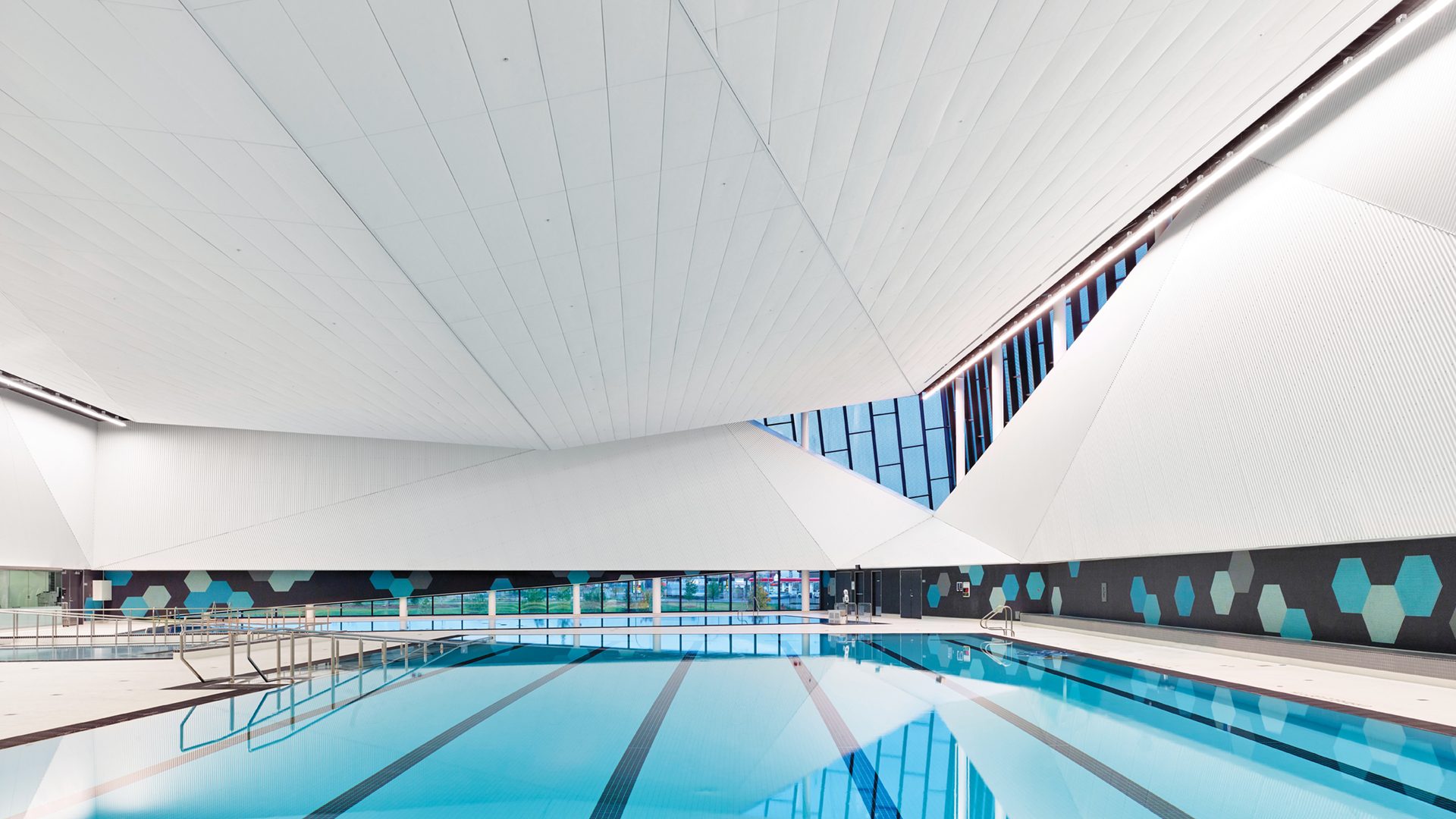 Modern indoor swimming pool with dramatic angled white ceiling system.
