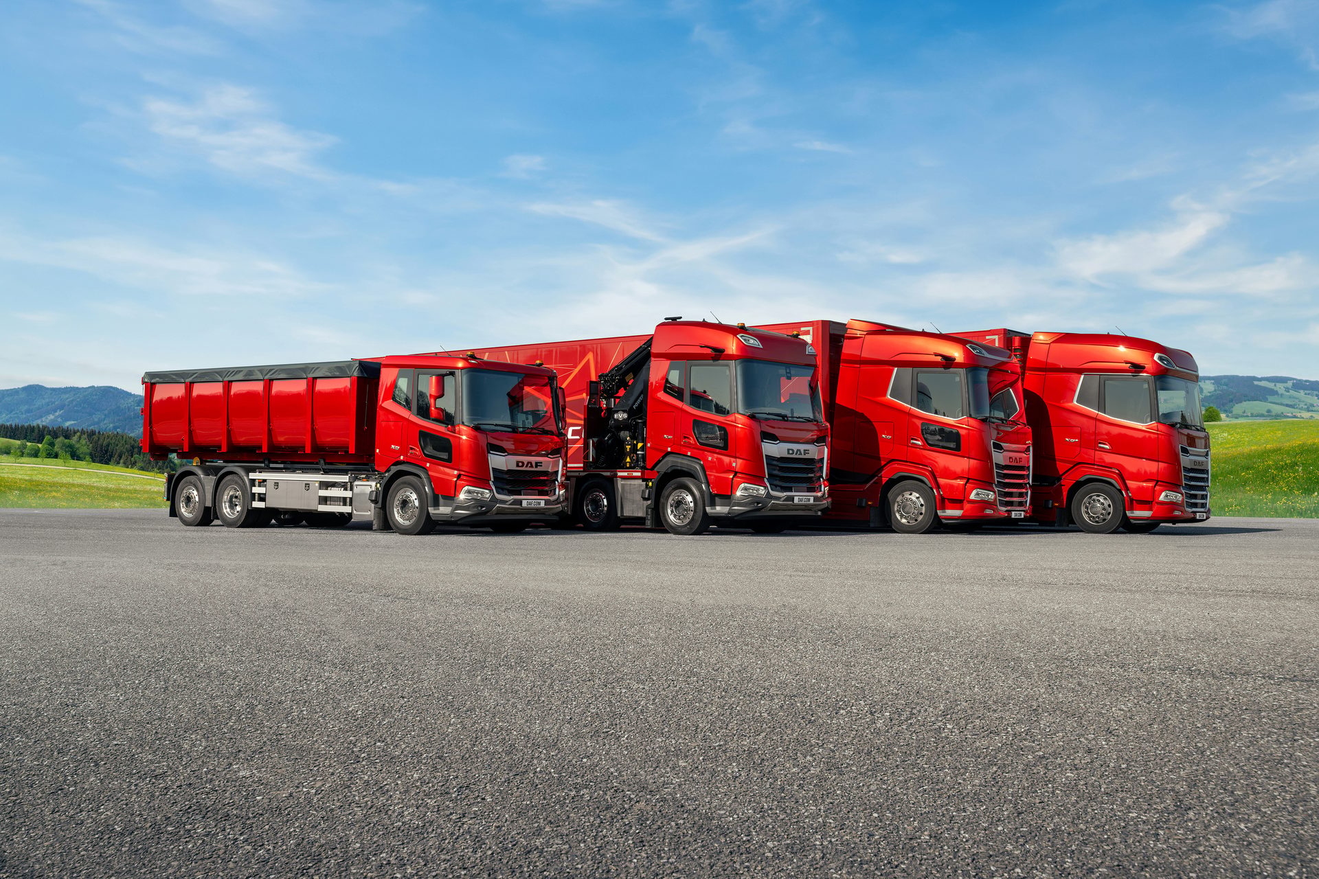 Four red DAF trucks of various models, including a dump truck and crane truck, parked on asphalt.