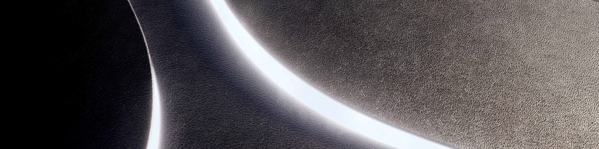 Abstract dark, textured (leather-like) surfaces separated by bright, curving lines of light.