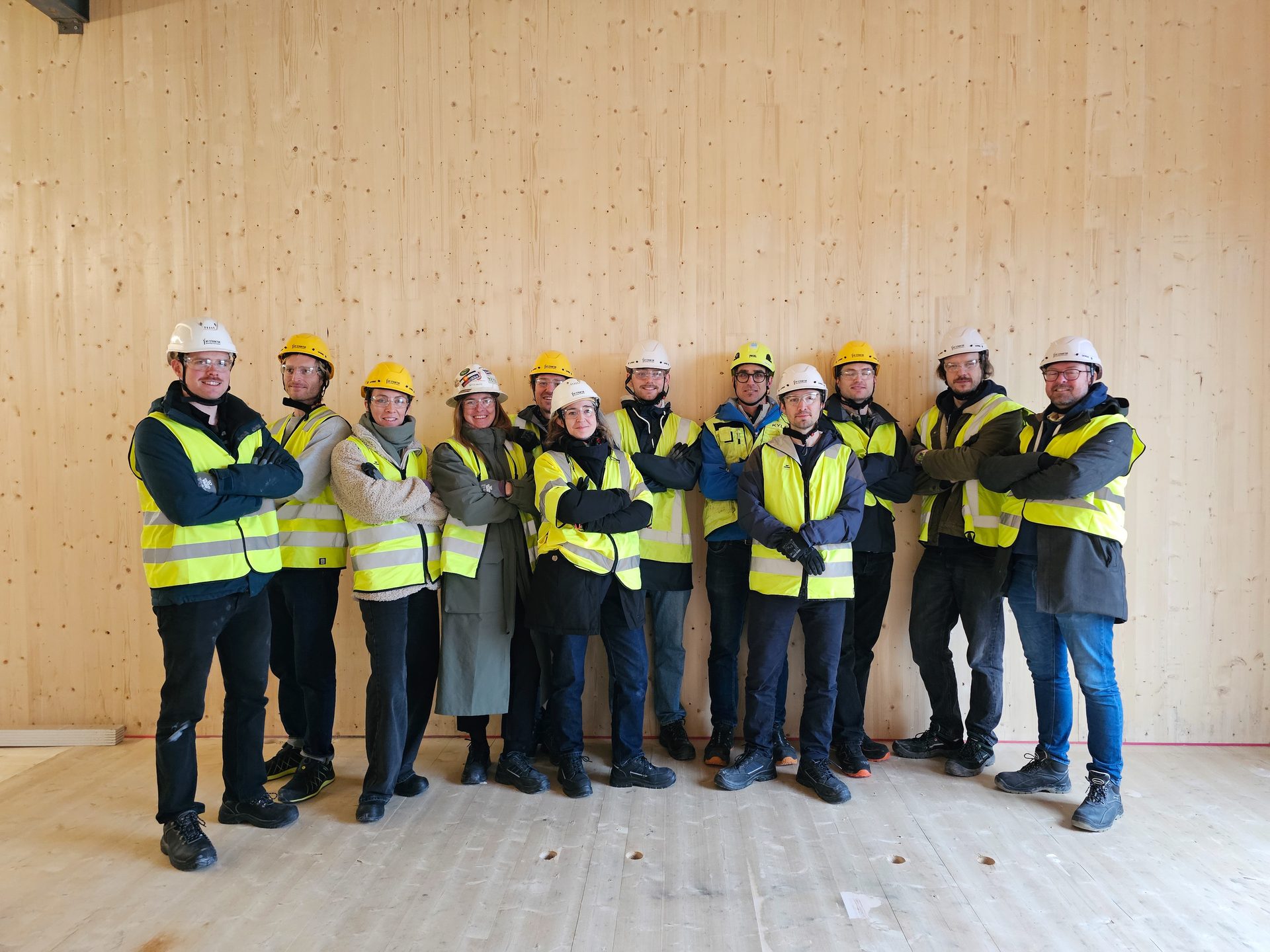 Gruppebilde av ingeniører fra Ny Struktur tatt på en byggeplass, foran en massivtre vegg