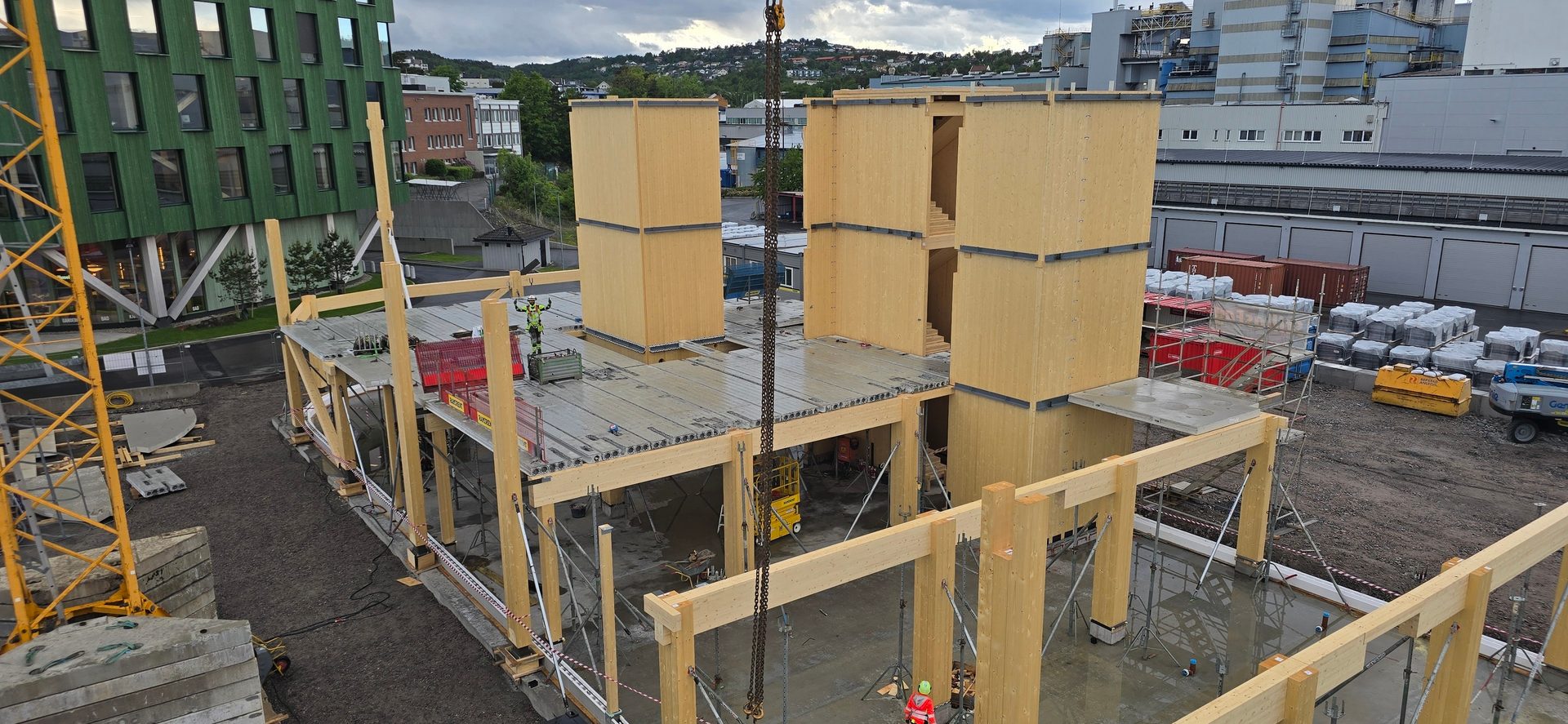 A multi-story timber building under construction with a crane and workers.