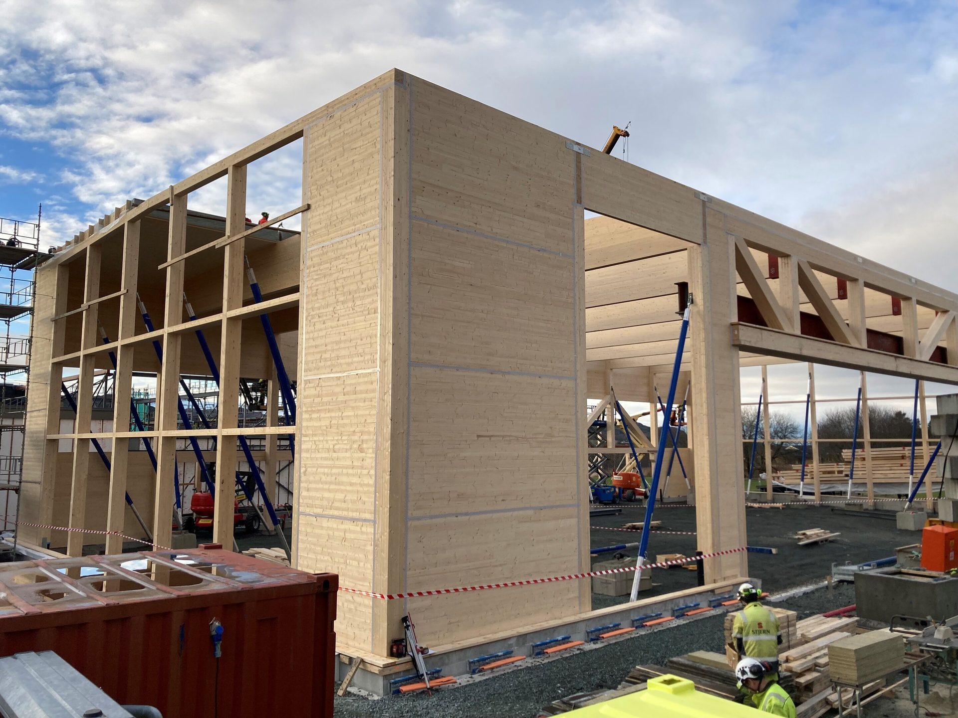 Large timber building under construction: exposed wooden frame, CLT walls, blue temporary supports.
