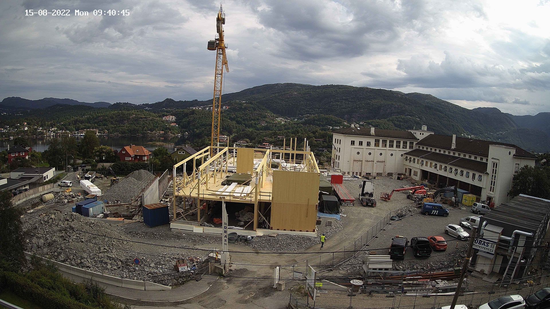 Timber building frame and crane at a construction site by mountains and water.