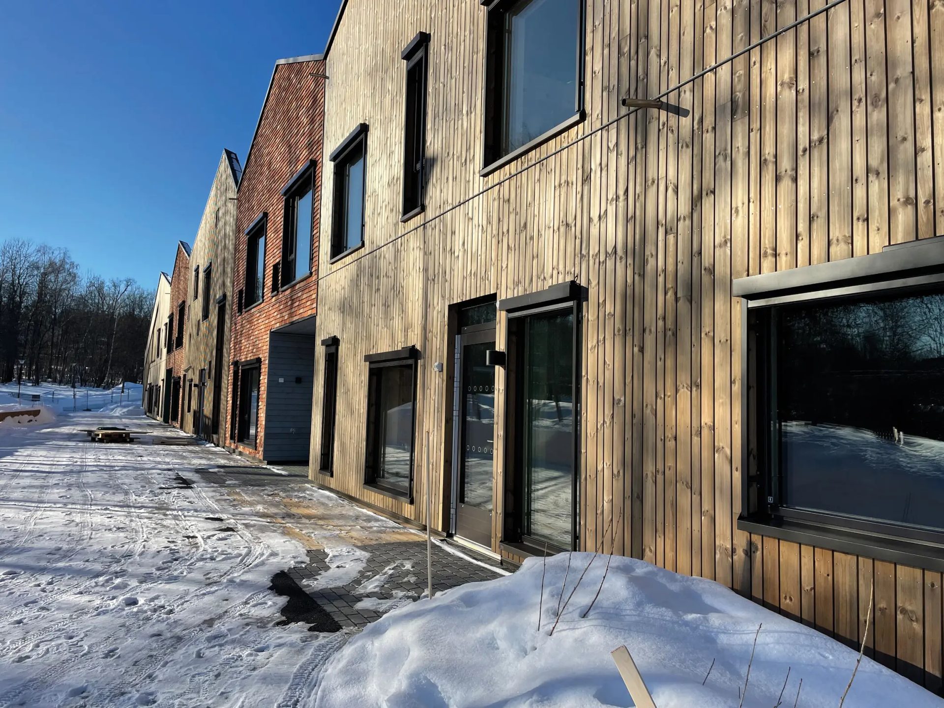 Modern wood and brick townhouses, snowy ground, blue sky.