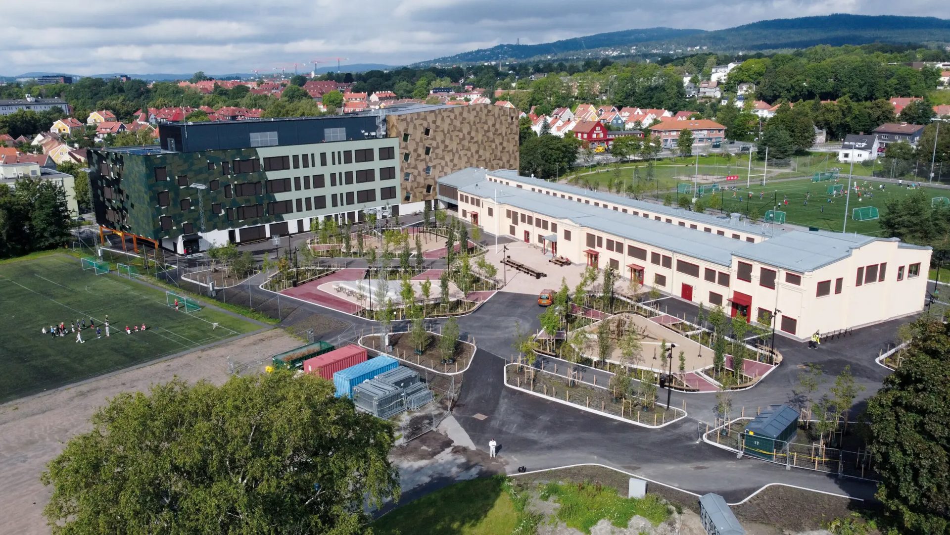 Aerial view of a school complex with modern and older buildings, playgrounds, and sports fields.