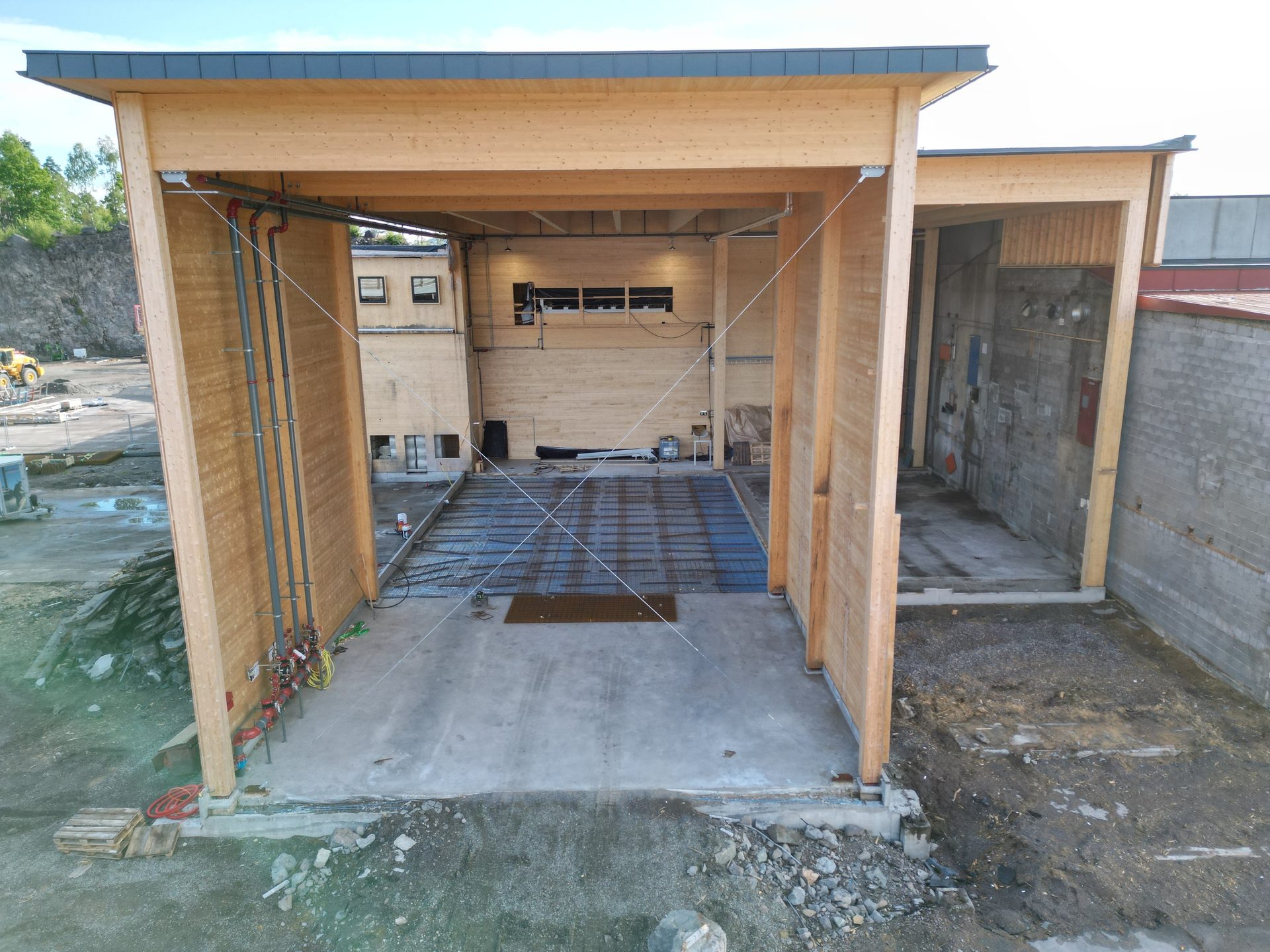 Open timber building under construction, possibly vehicle wash, with pipes and rebar.