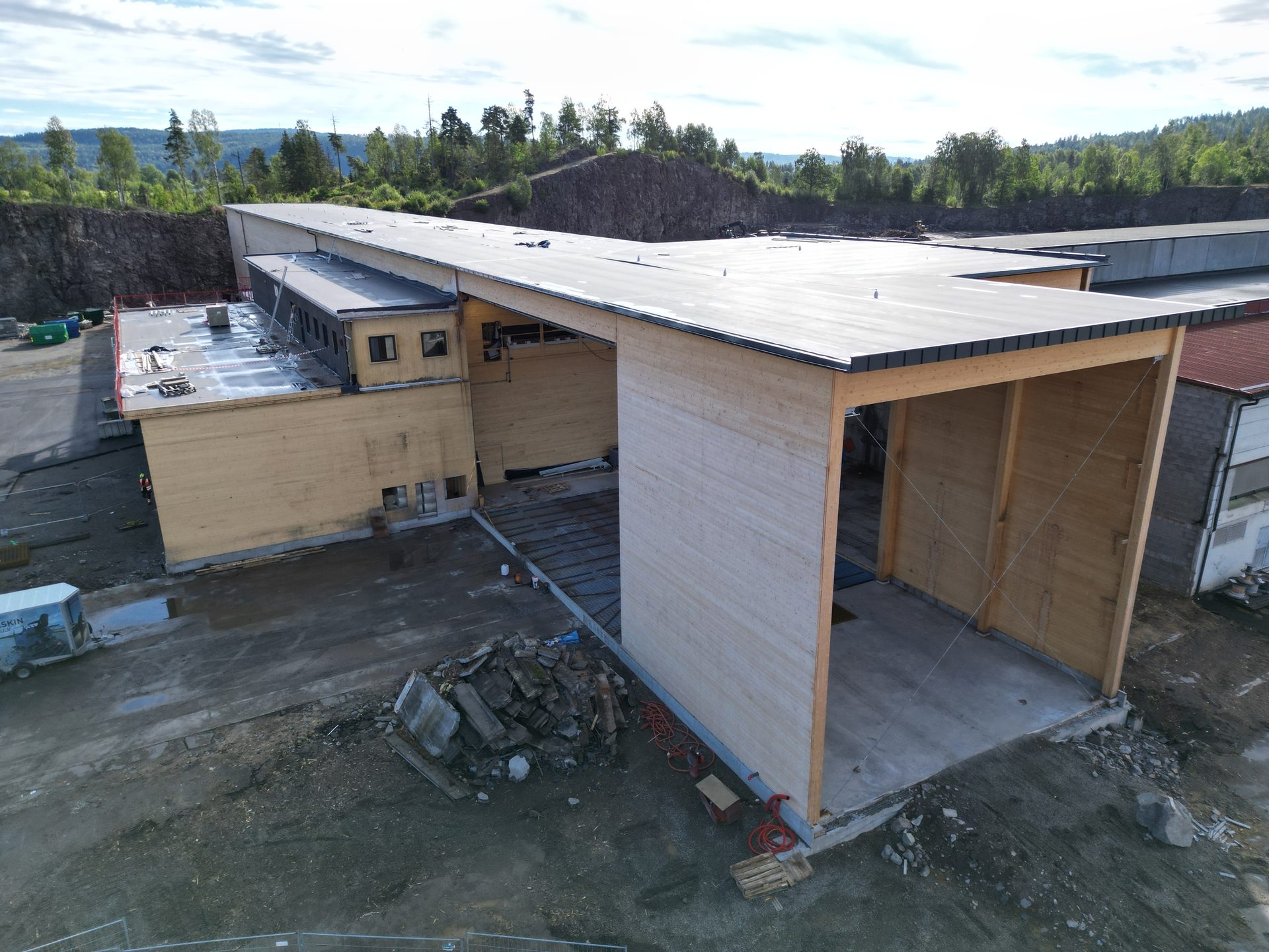 Modern wooden building under construction, with hills and forest in the background.