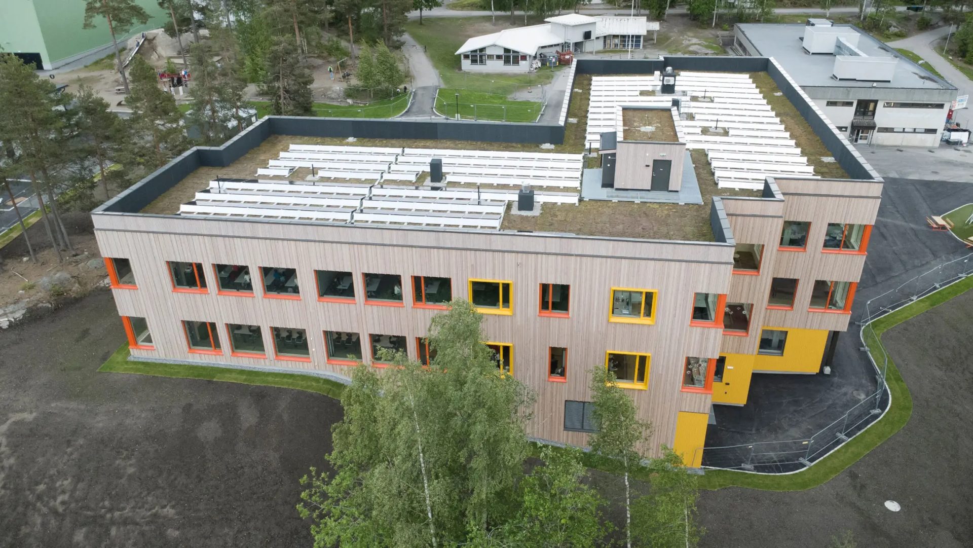 Aerial view of a modern wooden building with a green roof, solar panels, and colorful windows.