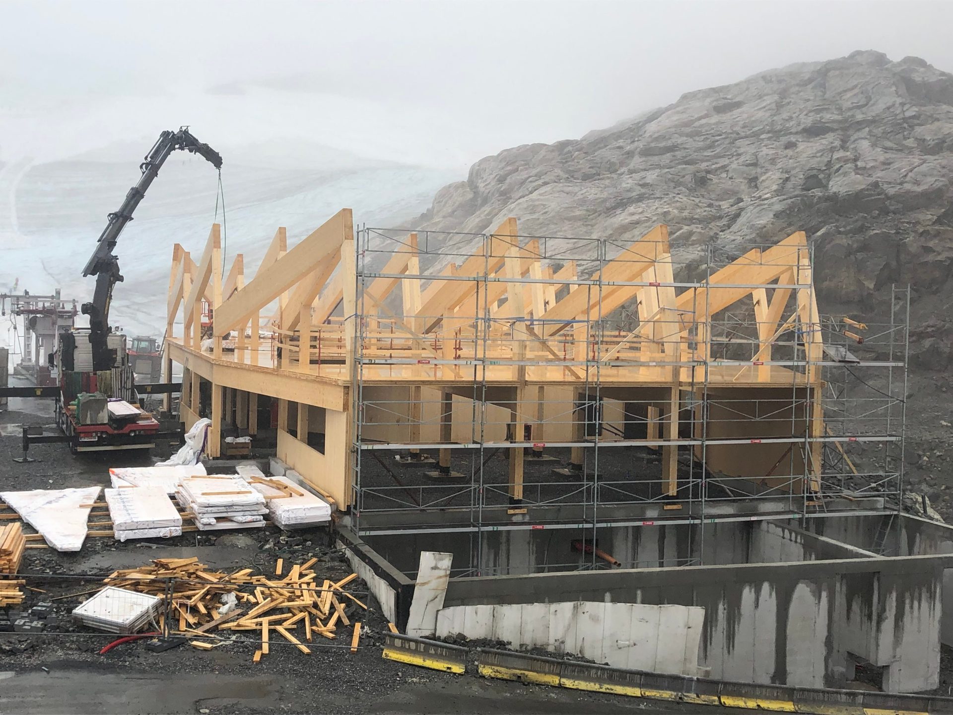 Timber building under construction on a misty mountain, with a crane and scaffolding.