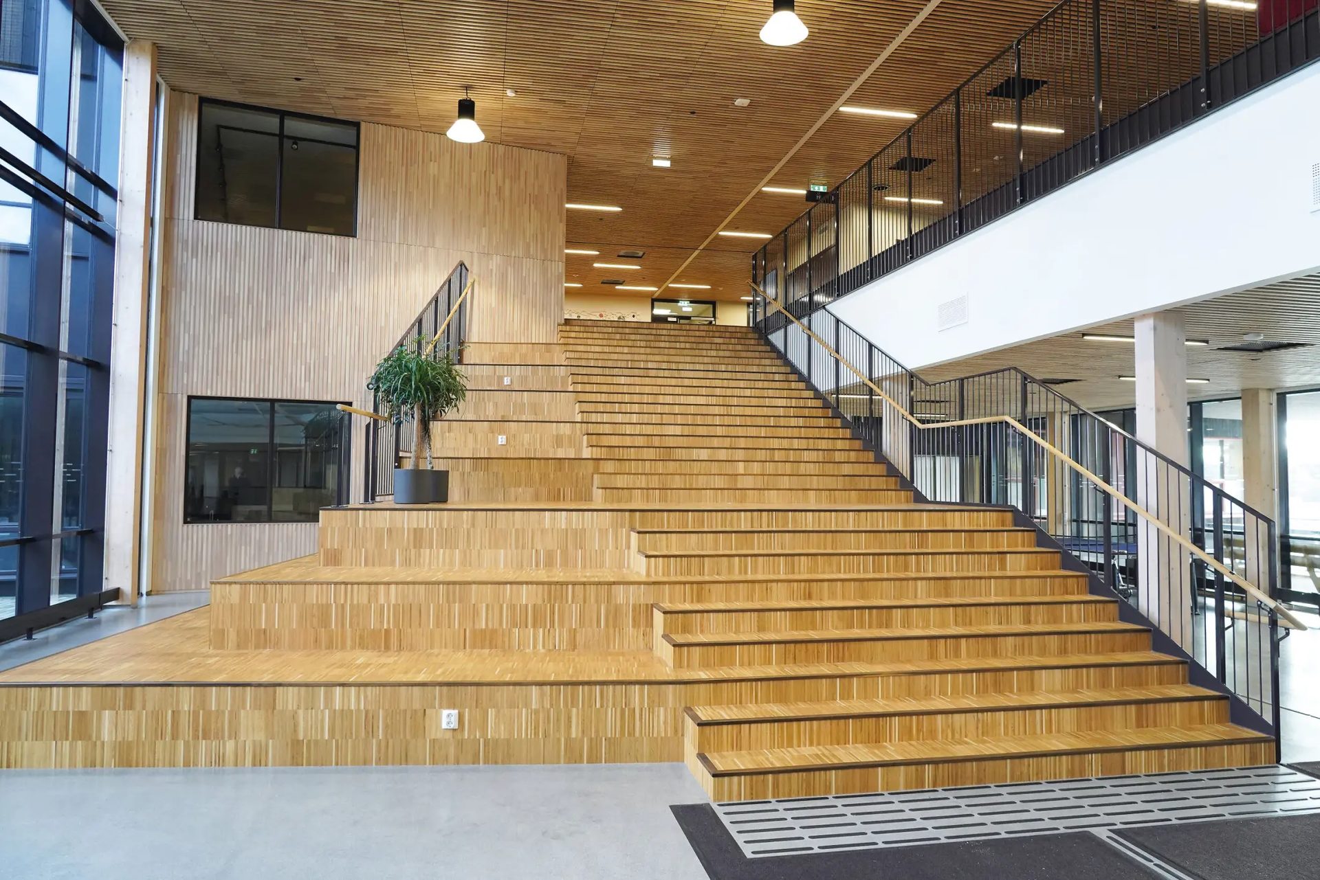 A modern, grand interior staircase with light wooden steps, wide seating areas, and metal railings.