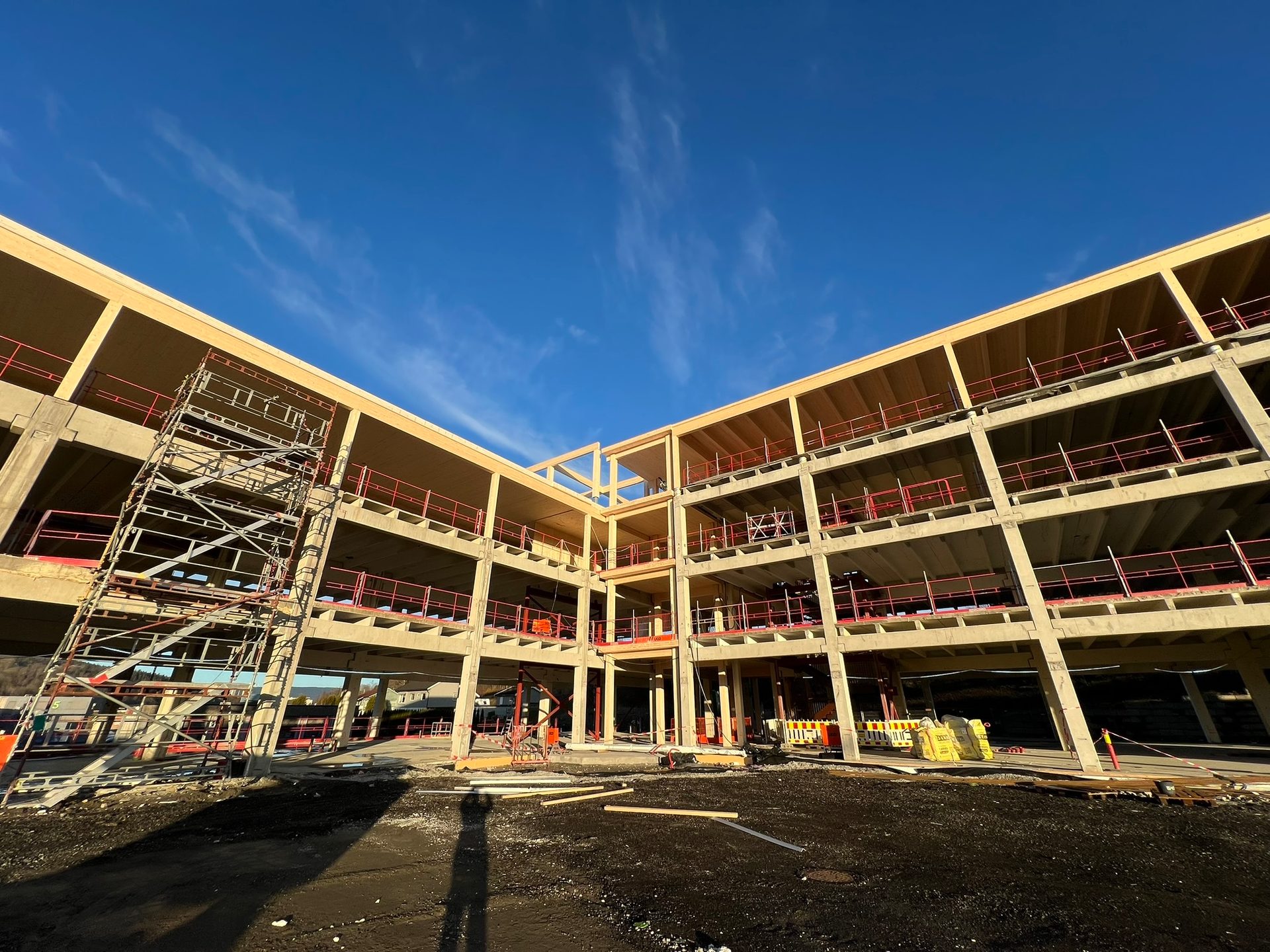 Large building under construction with concrete frame, wooden floors, scaffolding, under blue sky.