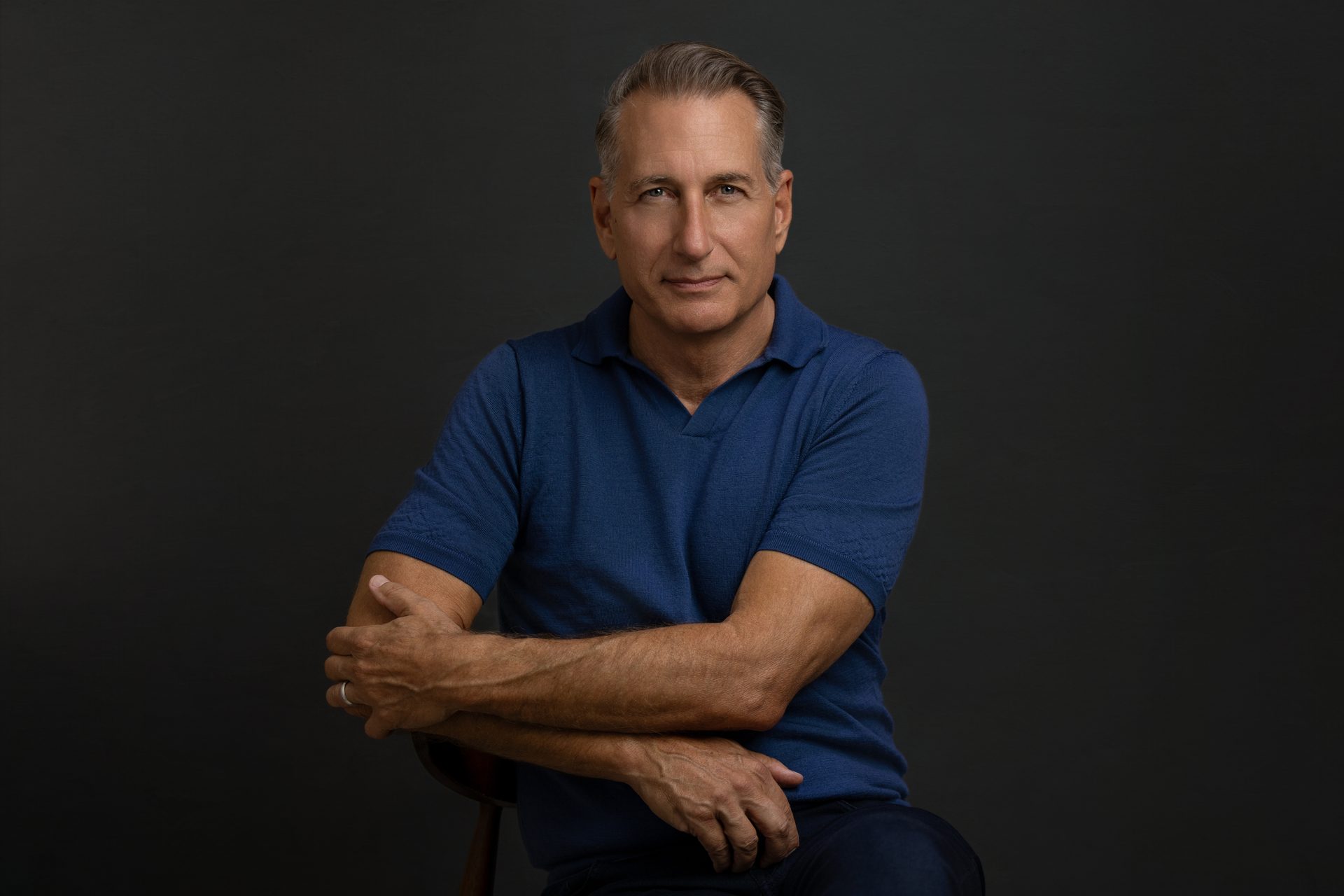 Portrait of a man in a blue polo shirt, arms crossed, looking at the camera.