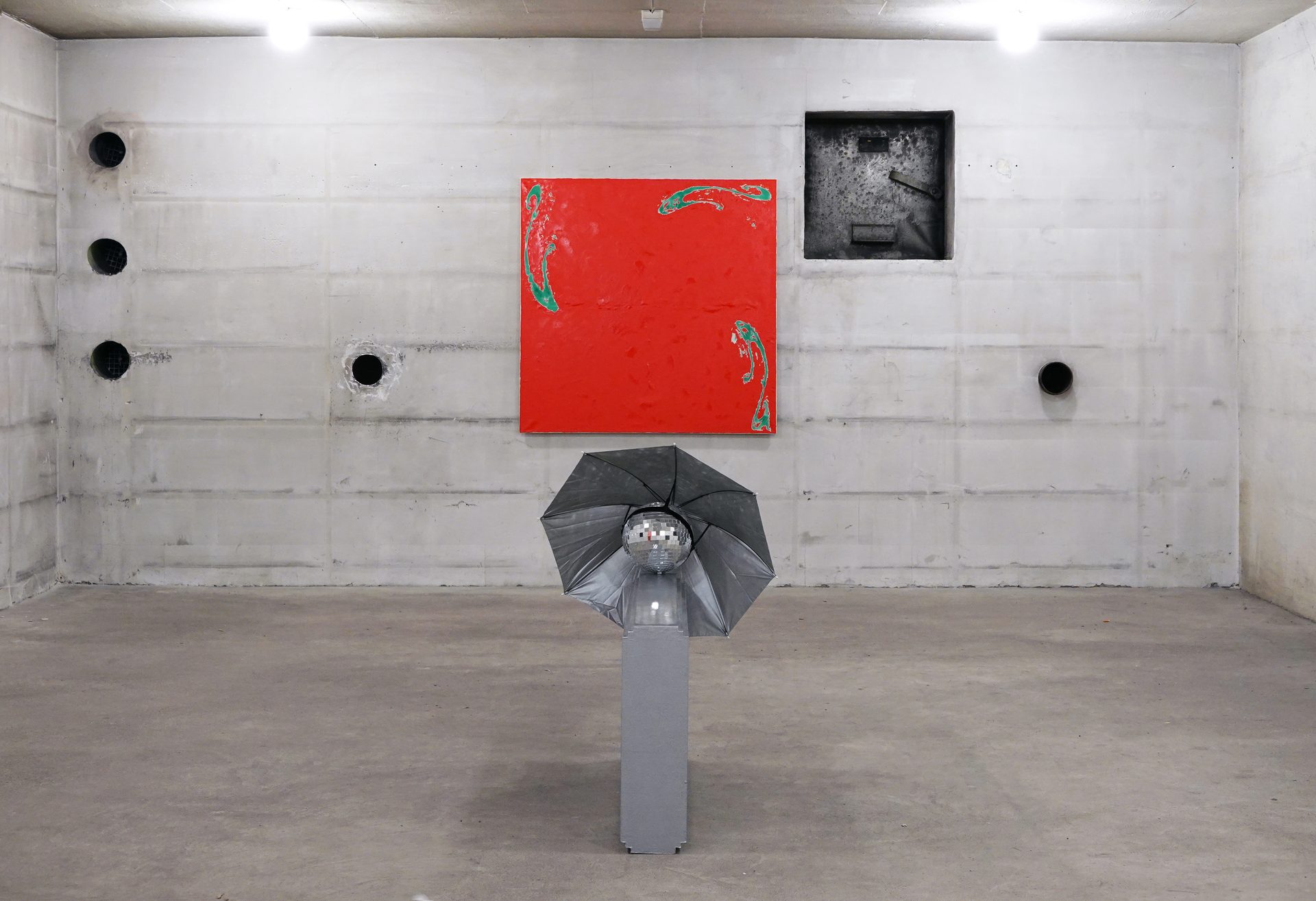 Art installation featuring a red painting and a disco ball with an umbrella reflector in a concrete room.