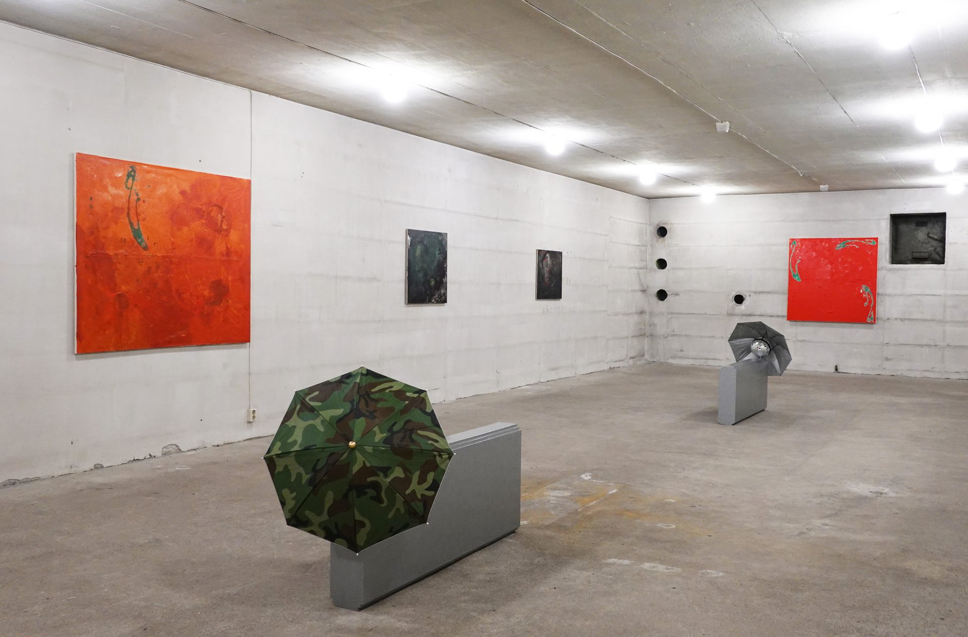 Art gallery with concrete walls, featuring abstract paintings and umbrella sculptures.