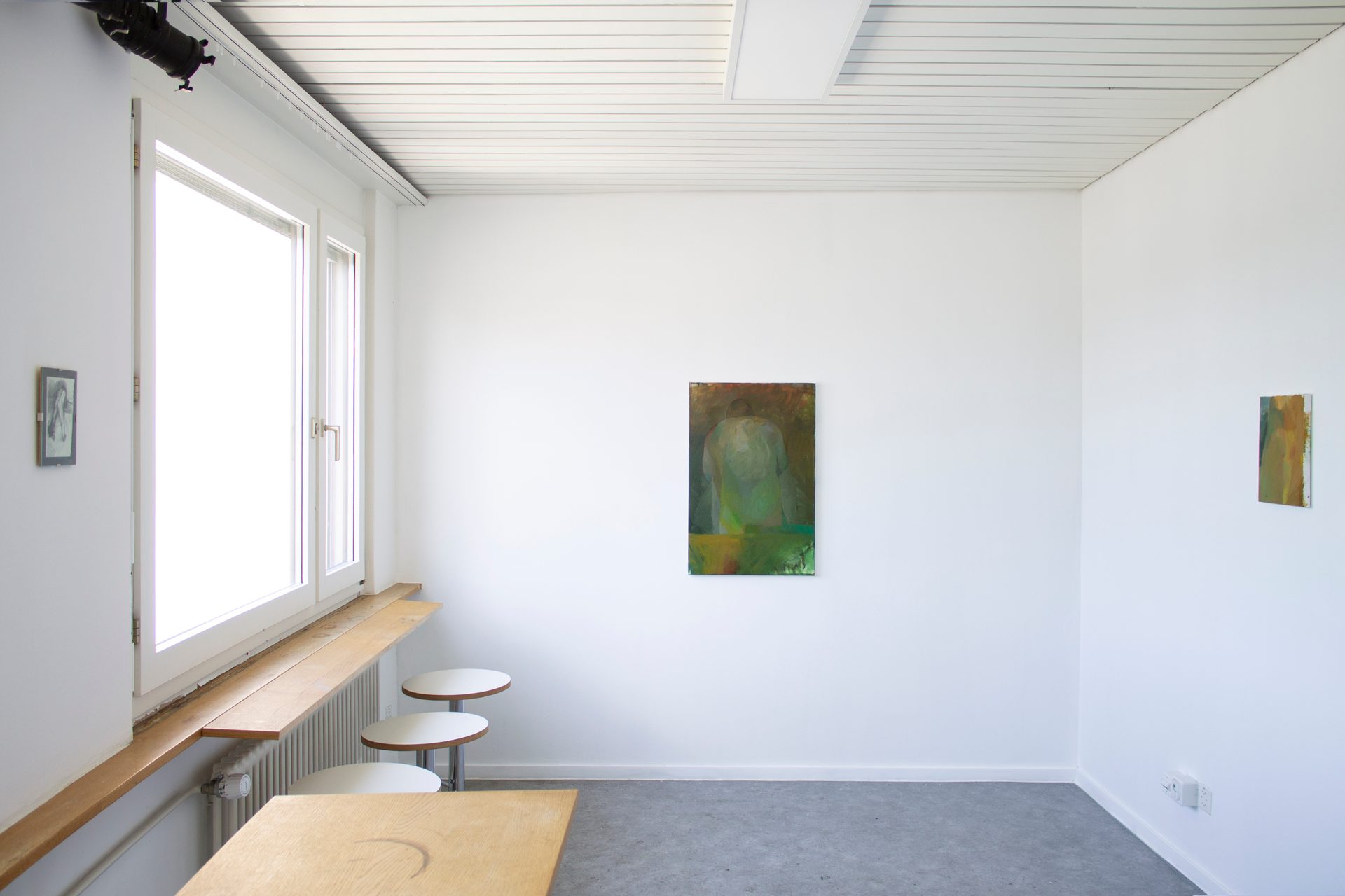 Bright room with white walls, a large window, wooden counter, white stools, and two abstract paintings.