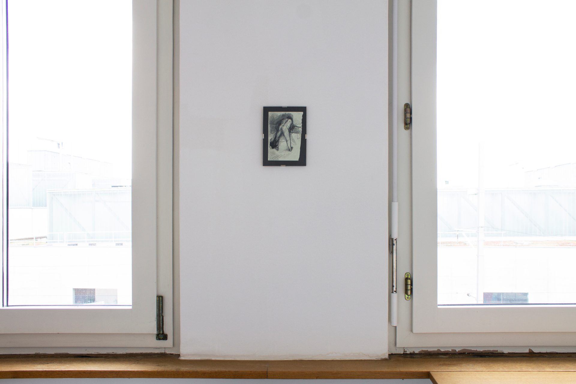 Small drawing of a bending figure on a white wall, framed by bright windows.