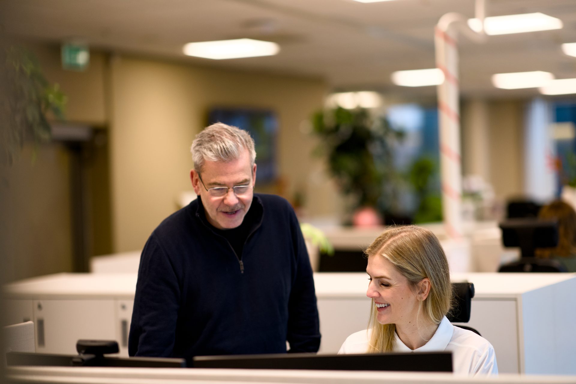 Man and woman smiling, collaborating at a desk in an office.