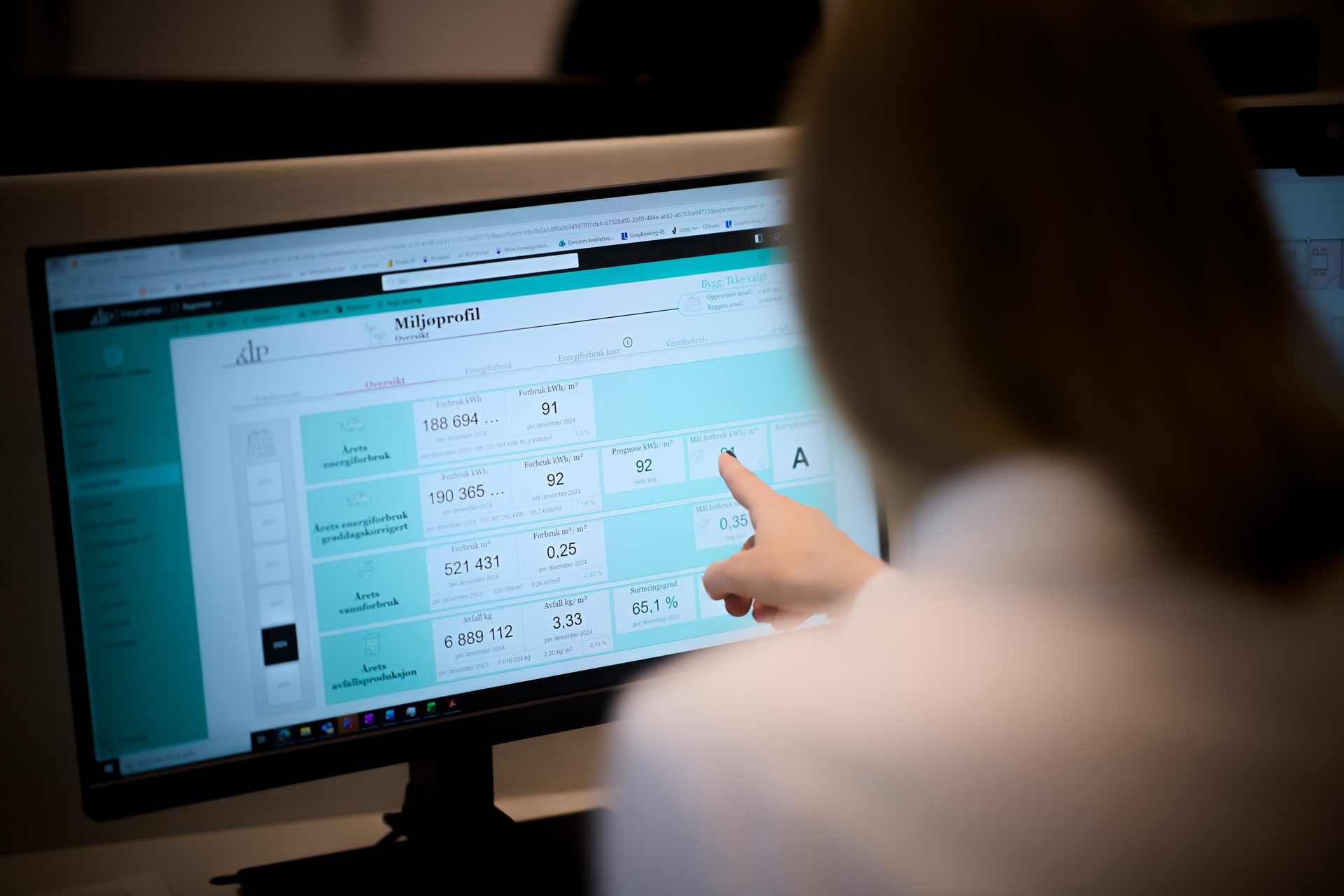 Person pointing at a "Miljøprofil" (Environmental Profile) dashboard on a computer screen.